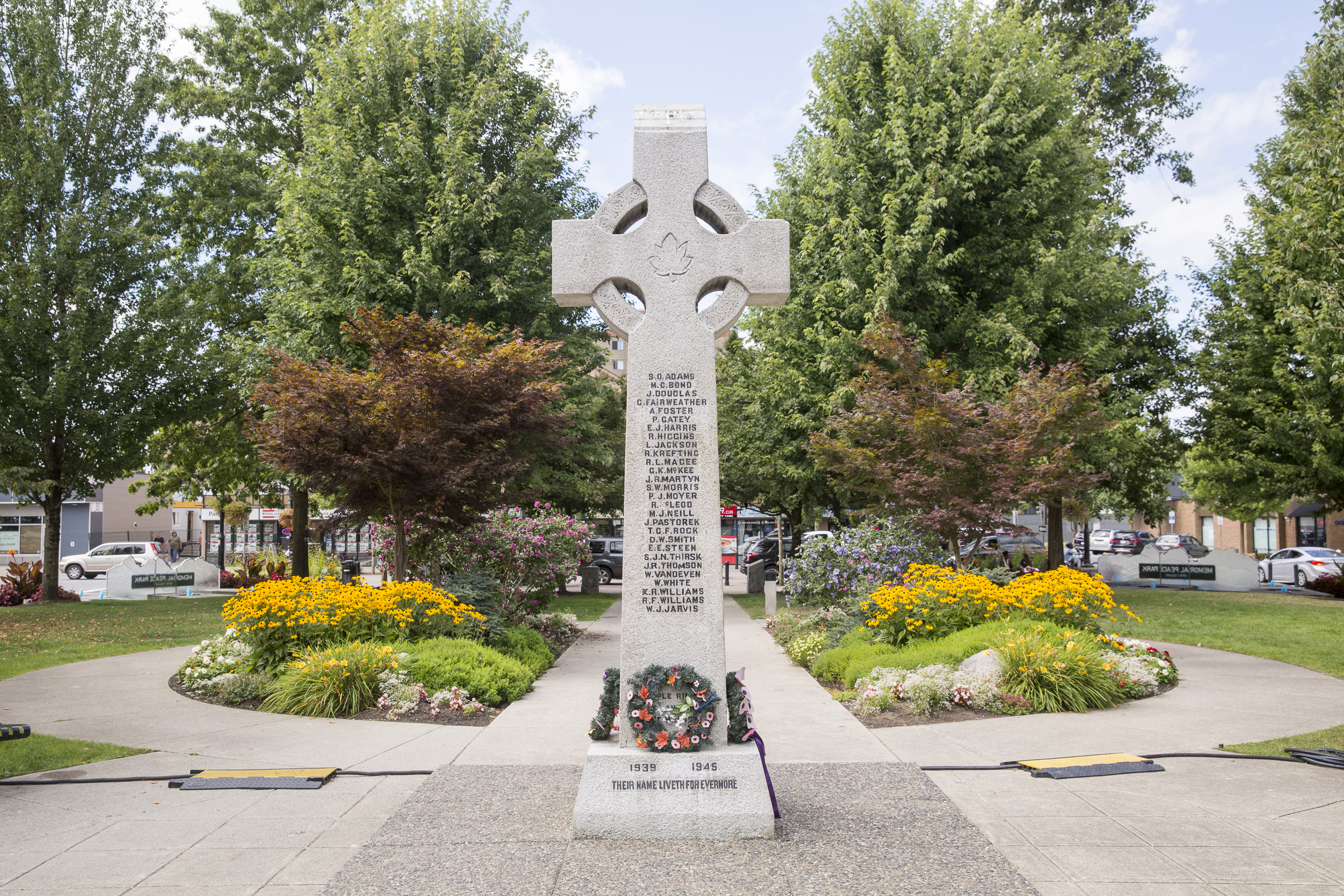 The Cenotaph at Memorial Peace Park stands tall with a small wreath set on its stand, and framed by flowers along the path behind it.