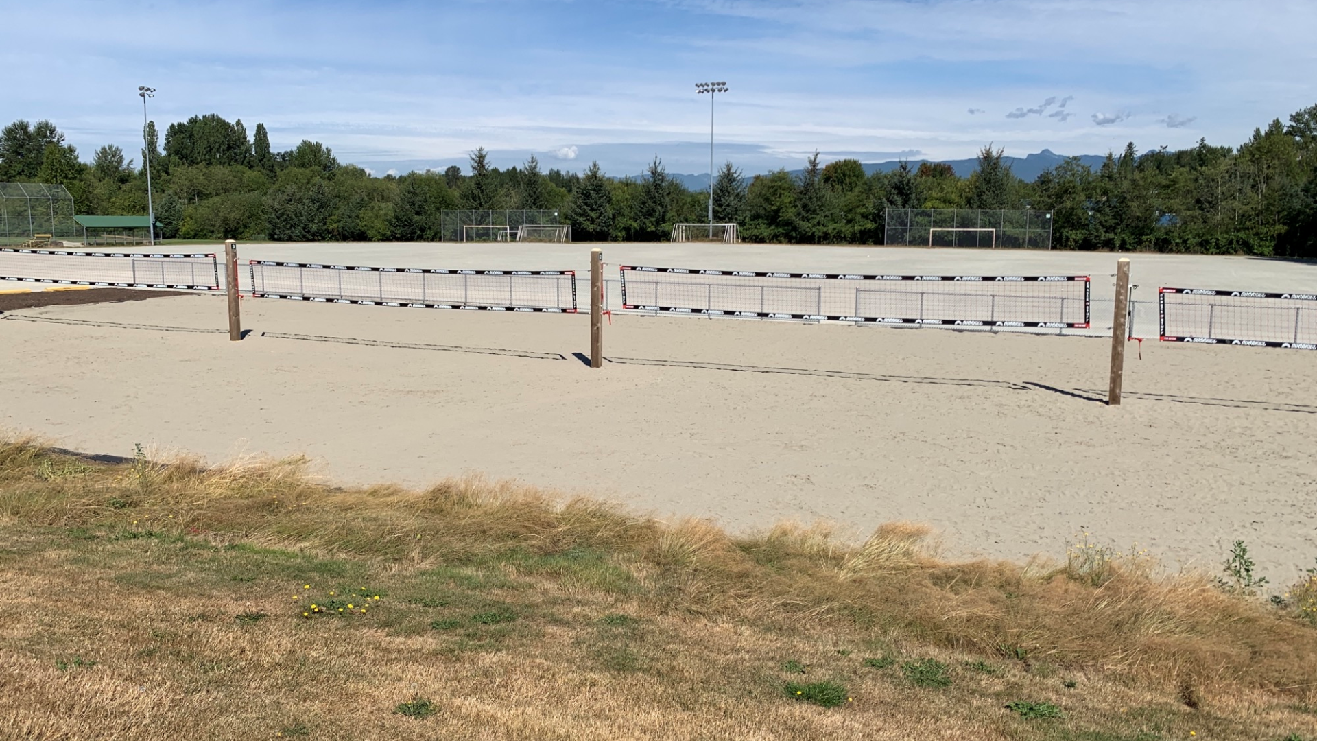 A few volleyball court on a sandy beach beside a field