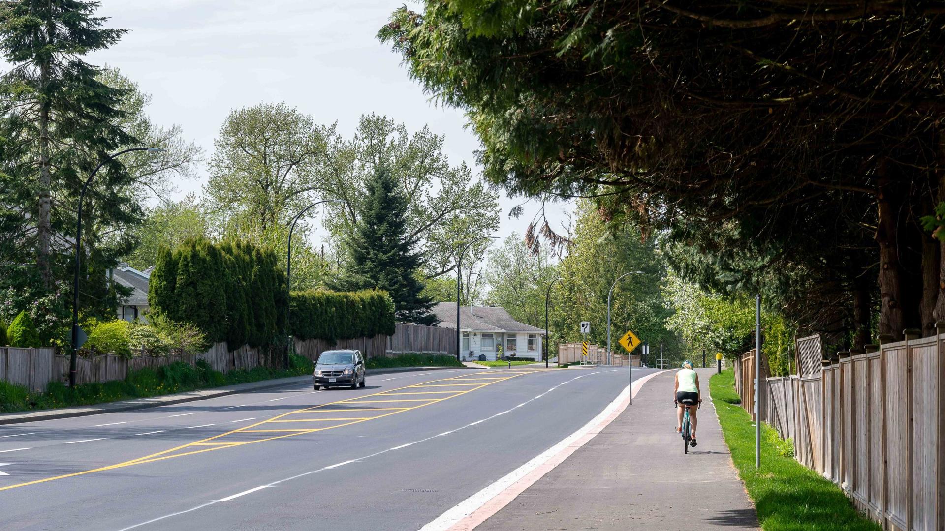 A wide, empty, freshly paved street. A biker uses the wide sidewalk.
