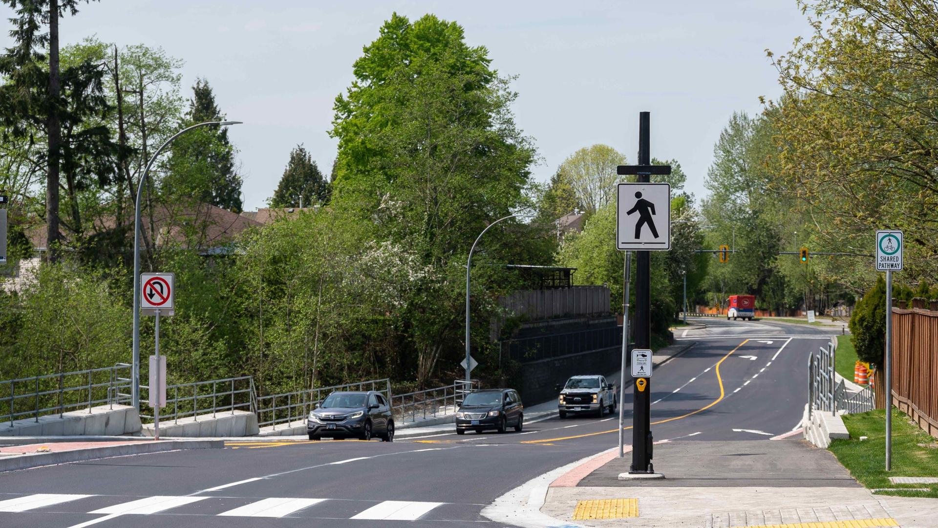 An uncontrolled pedestrian cross walk over a 4 lane road that's been freshly paved.