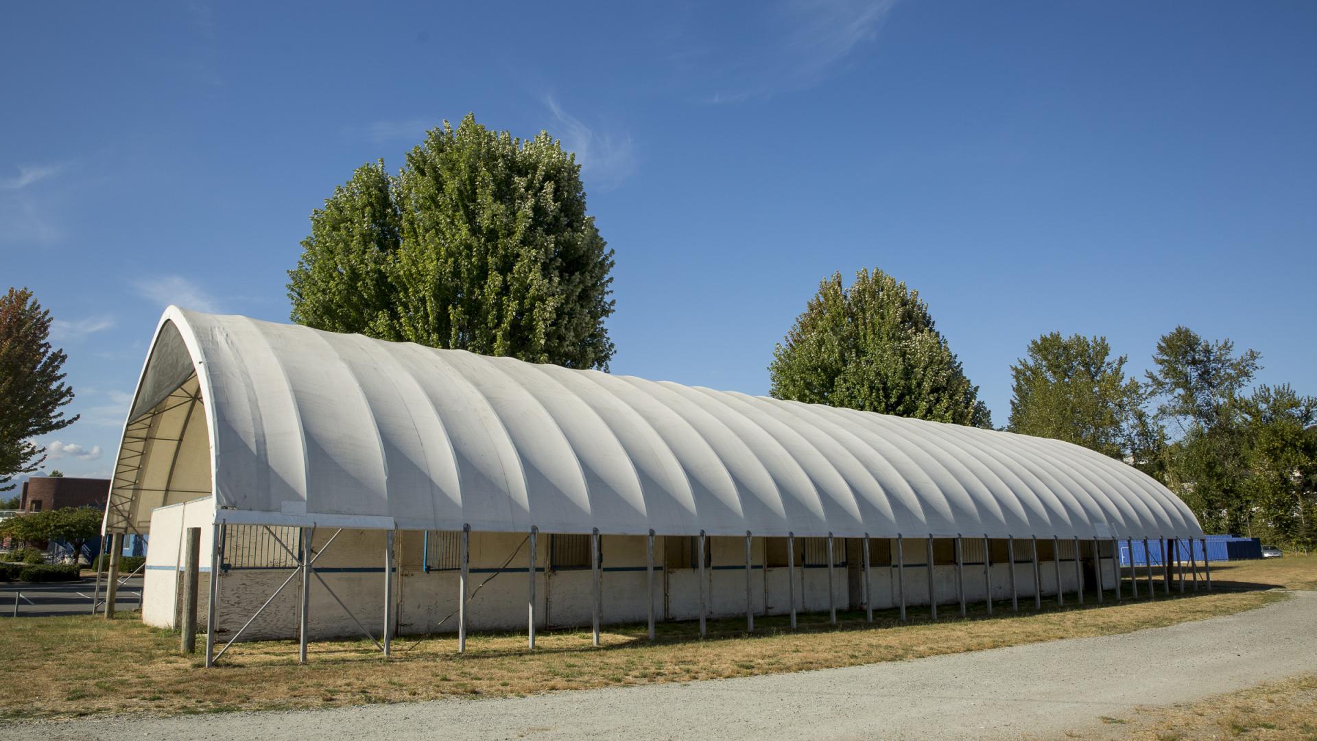 A cloth-covered open-air shelter sits on the Albion Fairgrounds, concealing horse stalls within.
