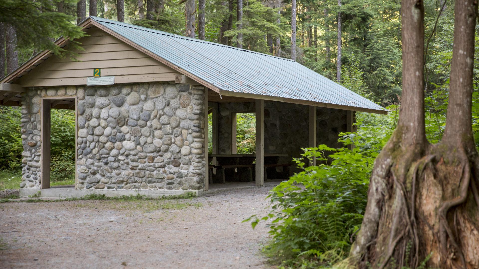 A picnic shelter with a stone accent wall is surrounded by the trees of the forest.