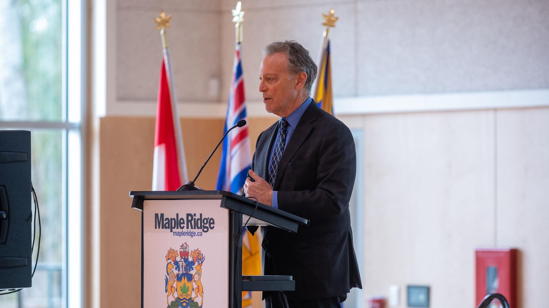 A man in a suit stands at a podium, delivering a speech.