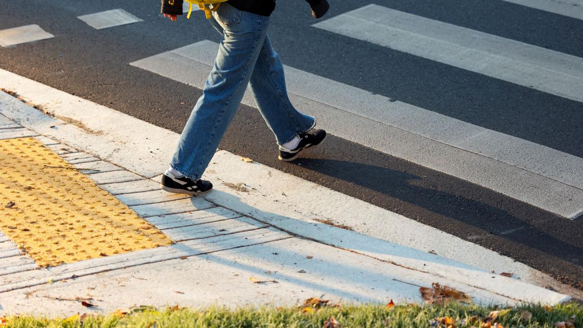 A person steps off the side walk, onto a marked crosswalk.