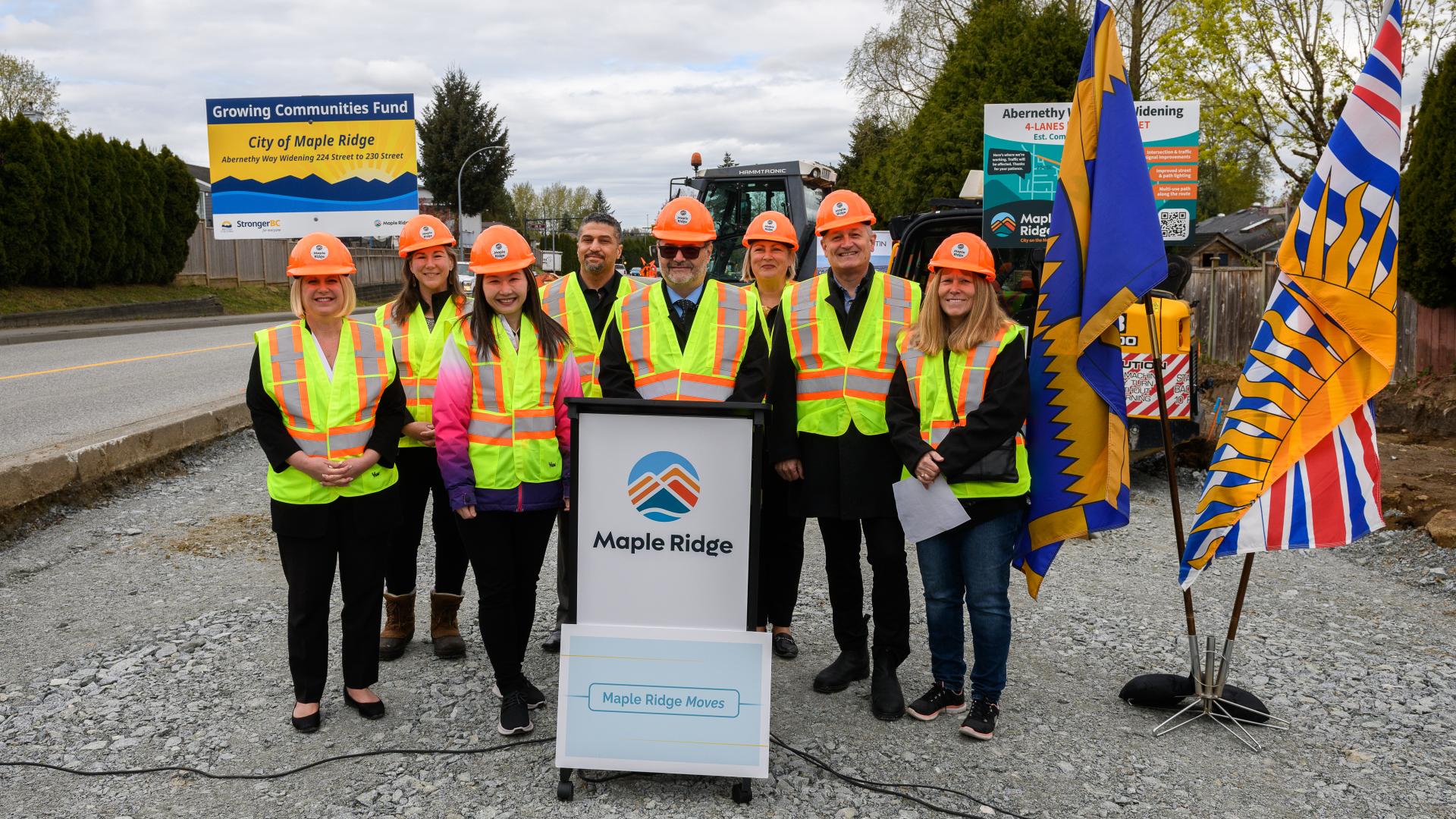 Mayor Dan Ruimy and others stand behind a podium in hard hats and high-visibility vests at the site of the Abernethy Way construction.