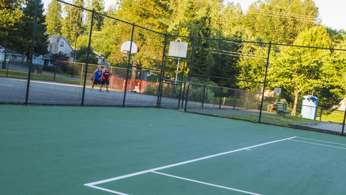 A green, fenced in sport pad. There are lines for a tennis court on the ground. 