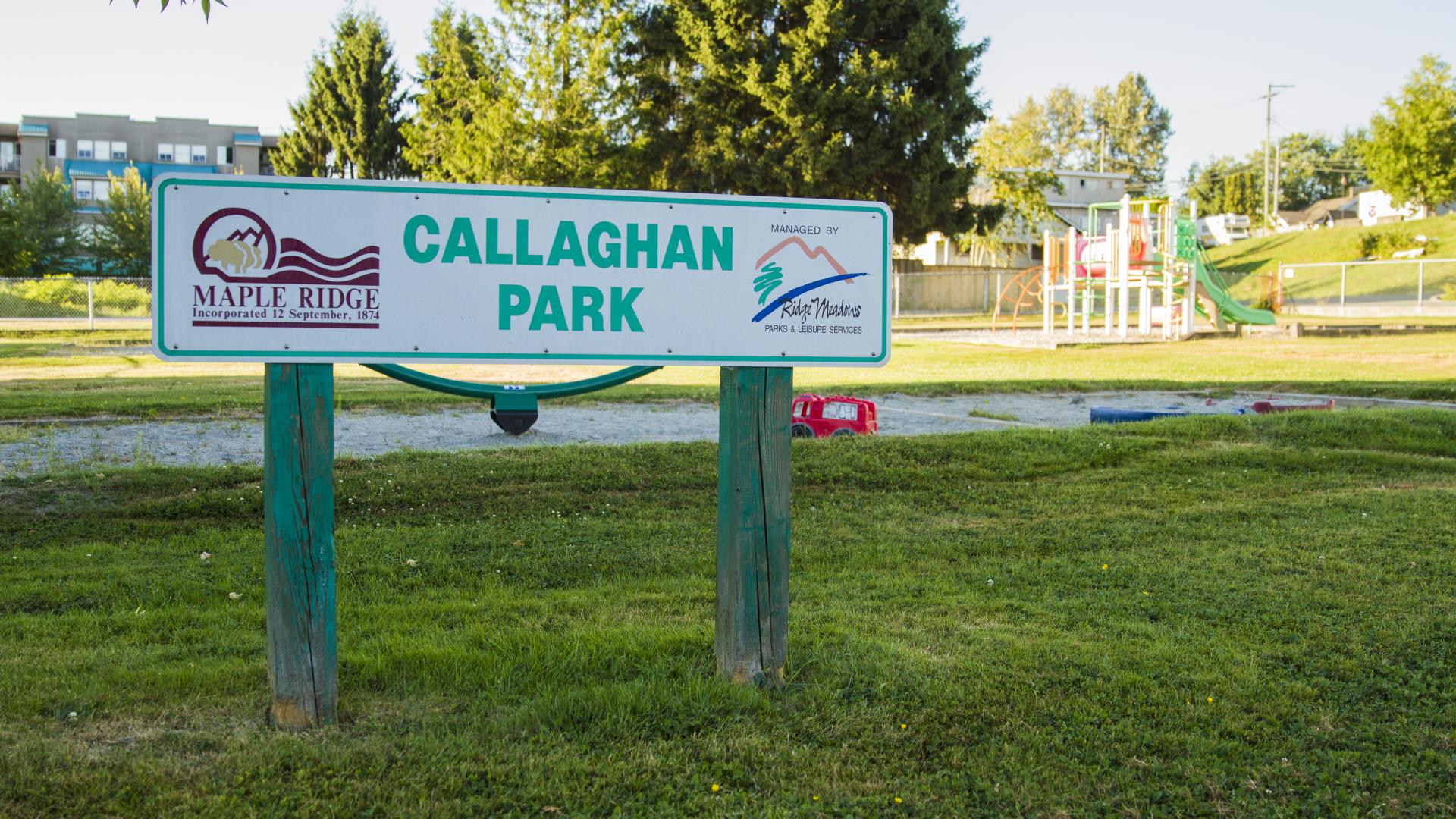 The Callaghan Park Sign. It stands in the grass and behind it is the parks playground.