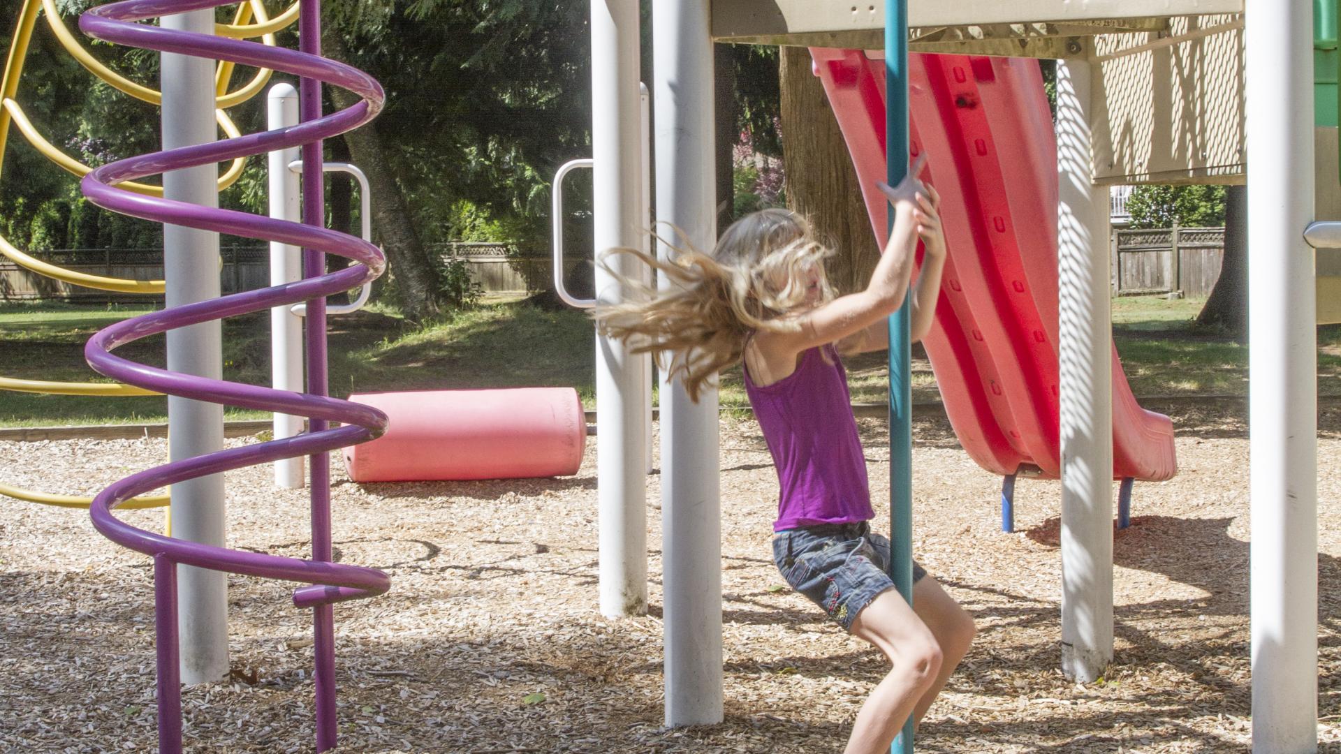 A young girl slides down a fire pole while a young boy climbs a spiral feature on a playground.