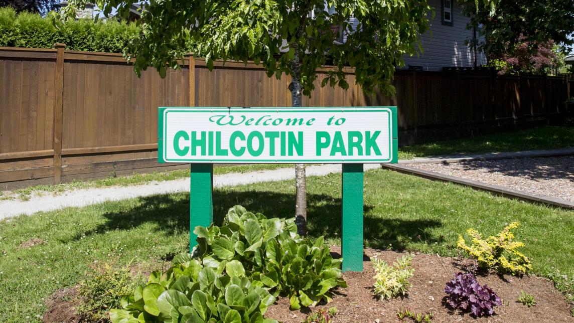 The Chilcotin Park sign in a garden with bushes.