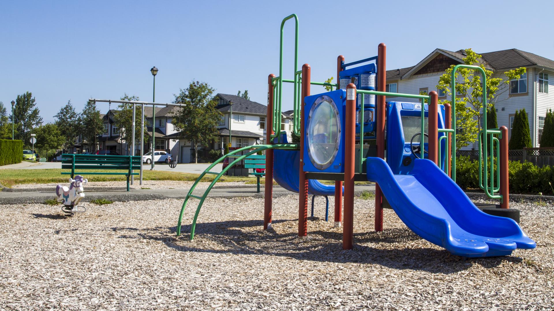 A small red, green and blue playground in a small park in a residential neighbourhood.