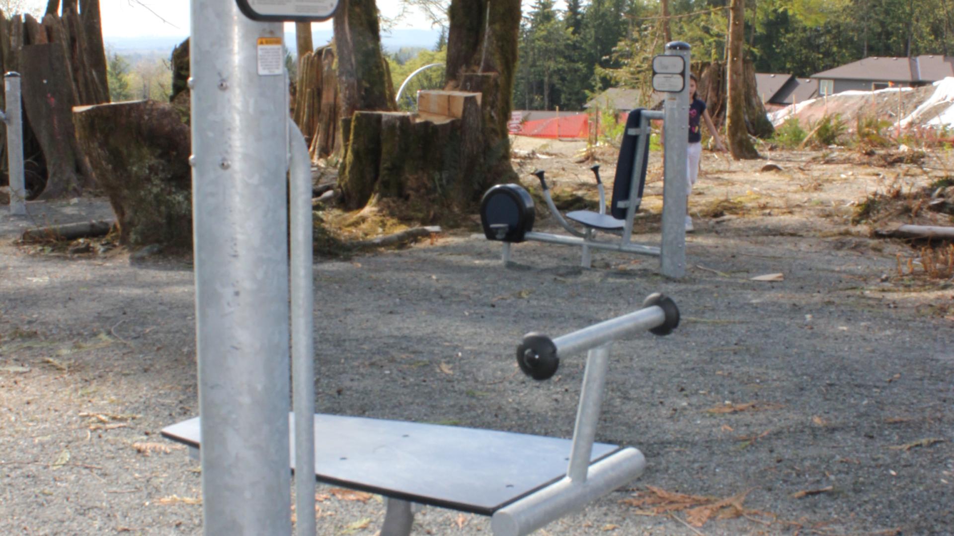 A piece of park workout equipment. There is a flat bench and a t-bar on one end. 
