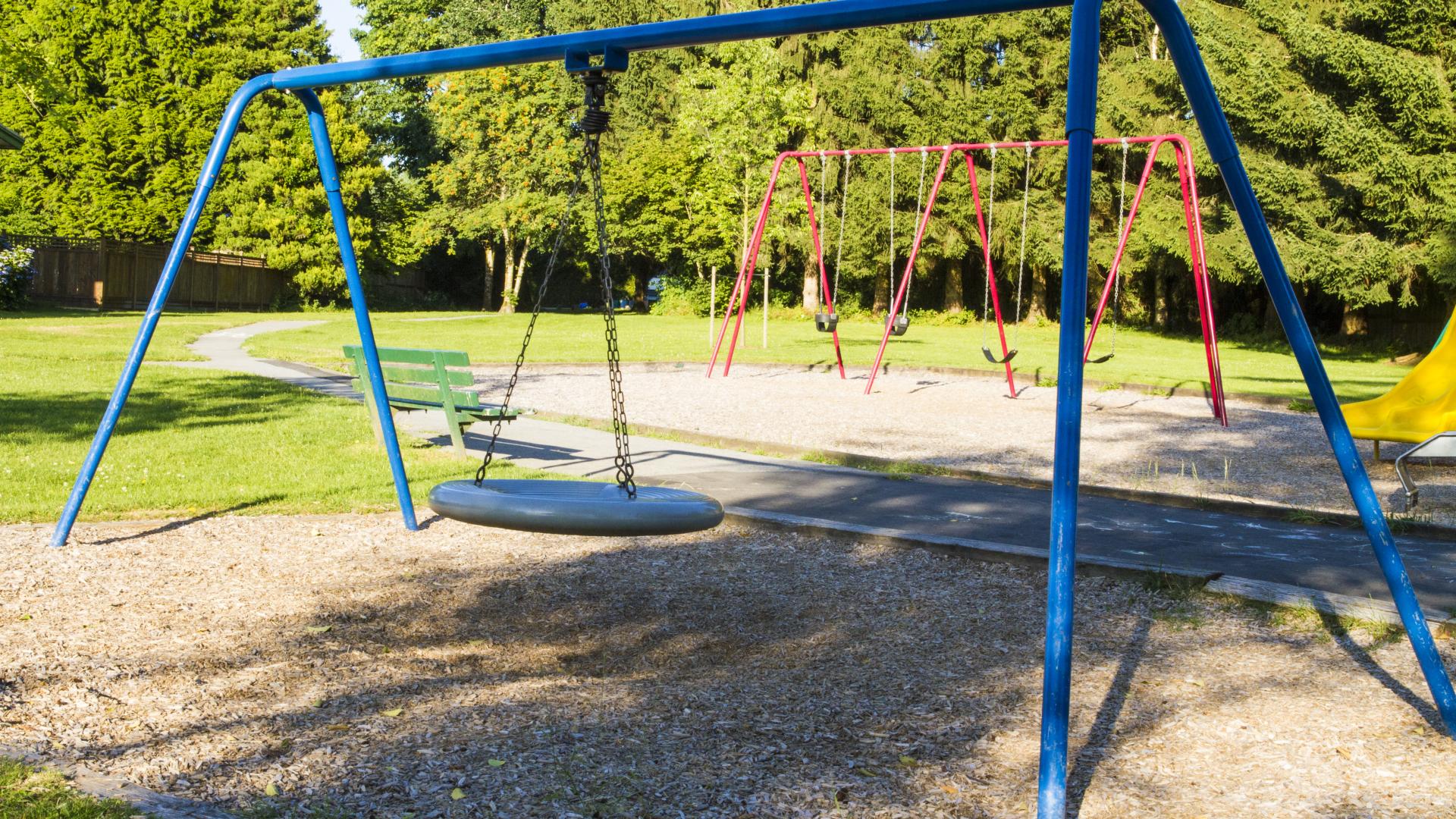 A set of swing sets, one have a large round disc to swing on.