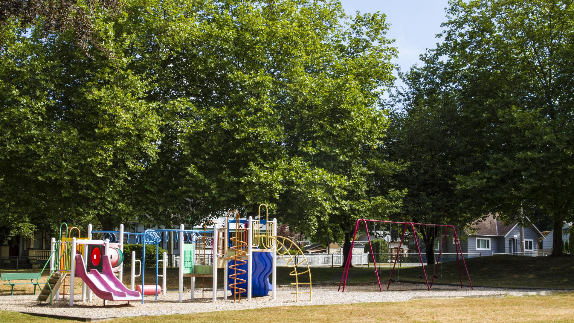 A short playground with a swing set. Trees line the back side of it.