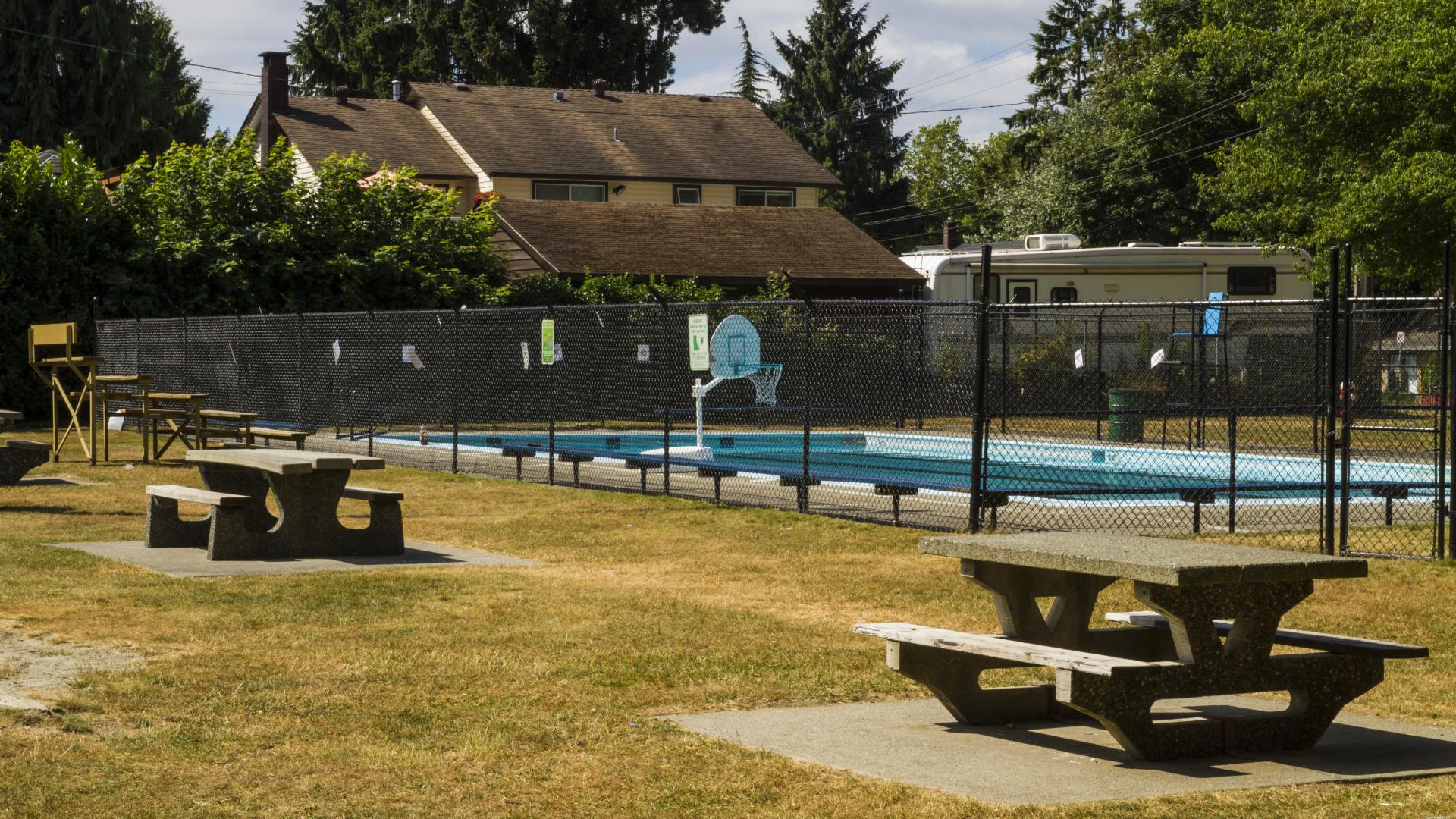 A fenced in pool. There are picnic tables in the grassy area around the pool fence.