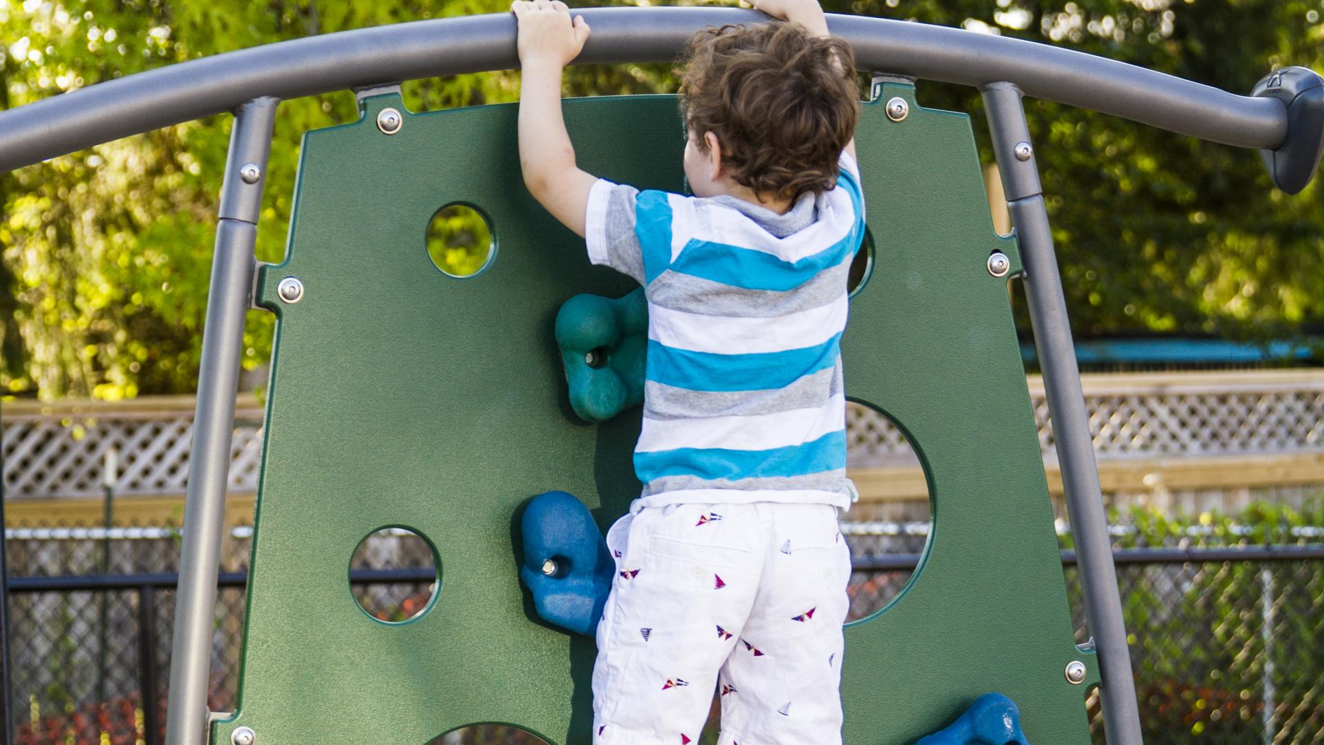 A toddler age boy pulls himself up on a small vertical rock climbing wall.