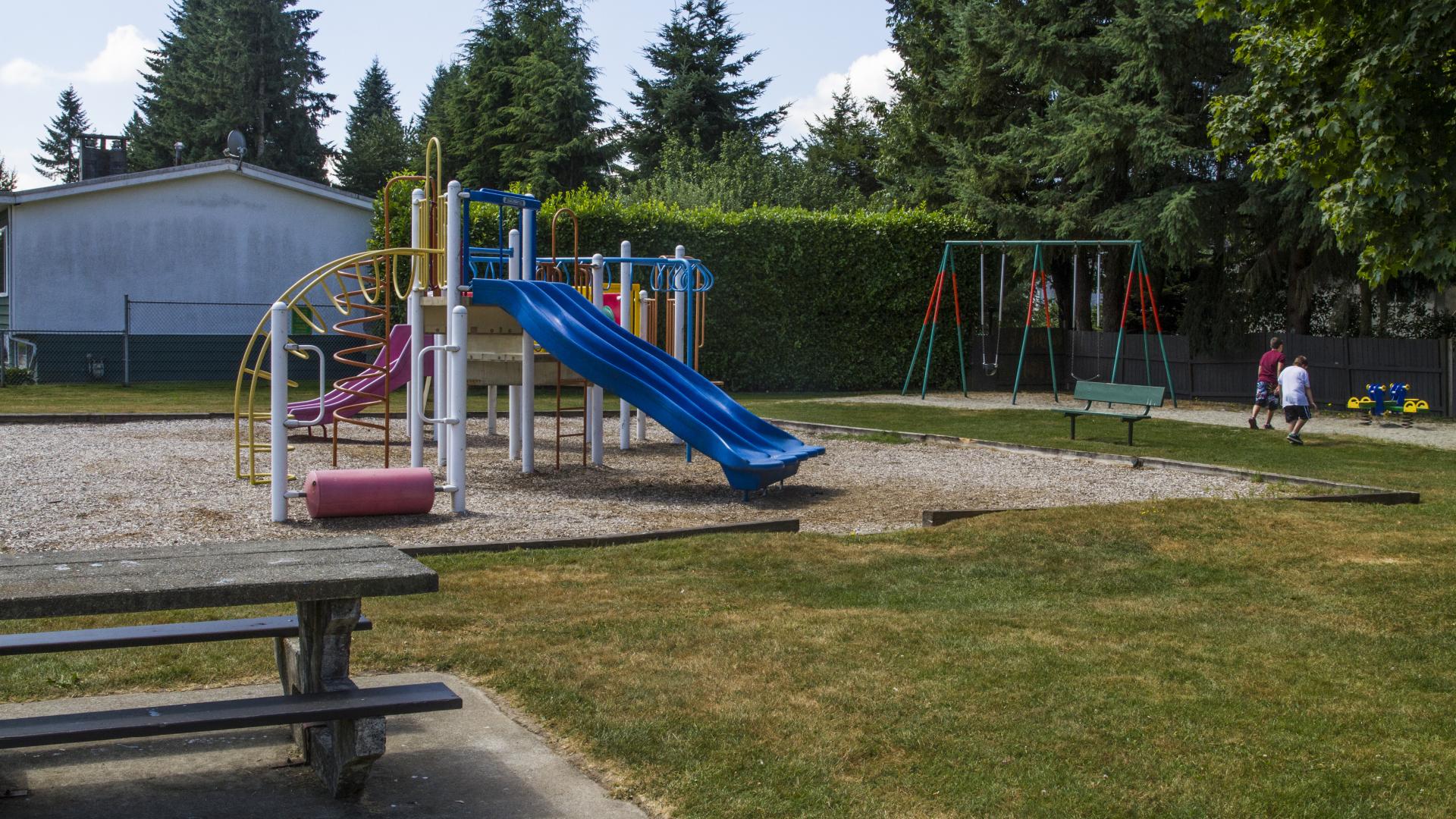 A picnic table sits close to the playground. From this angle, the swing set at the edge of the park is visible.