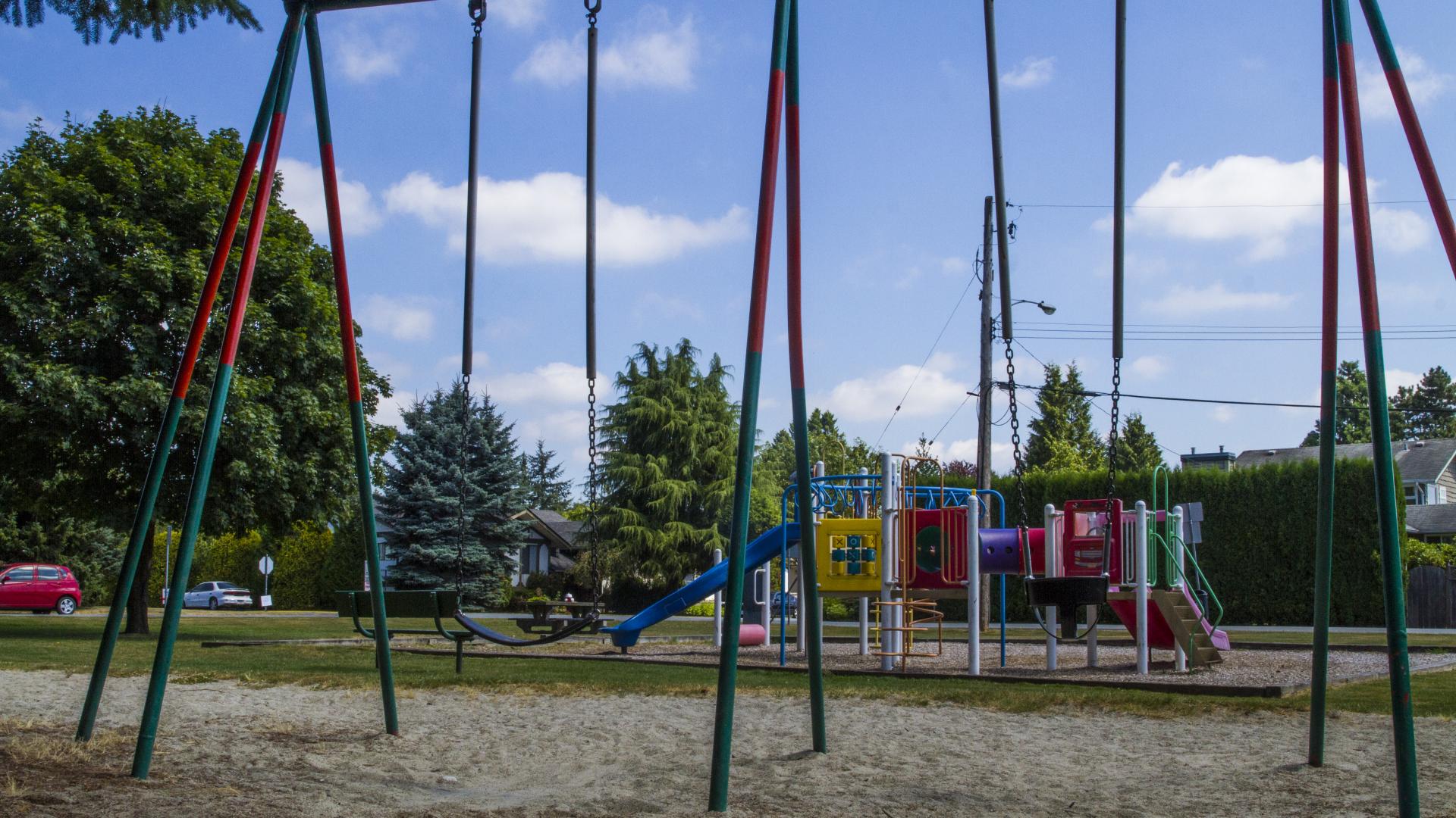 A swing set sits in the shade. A bit behind there is the playground.