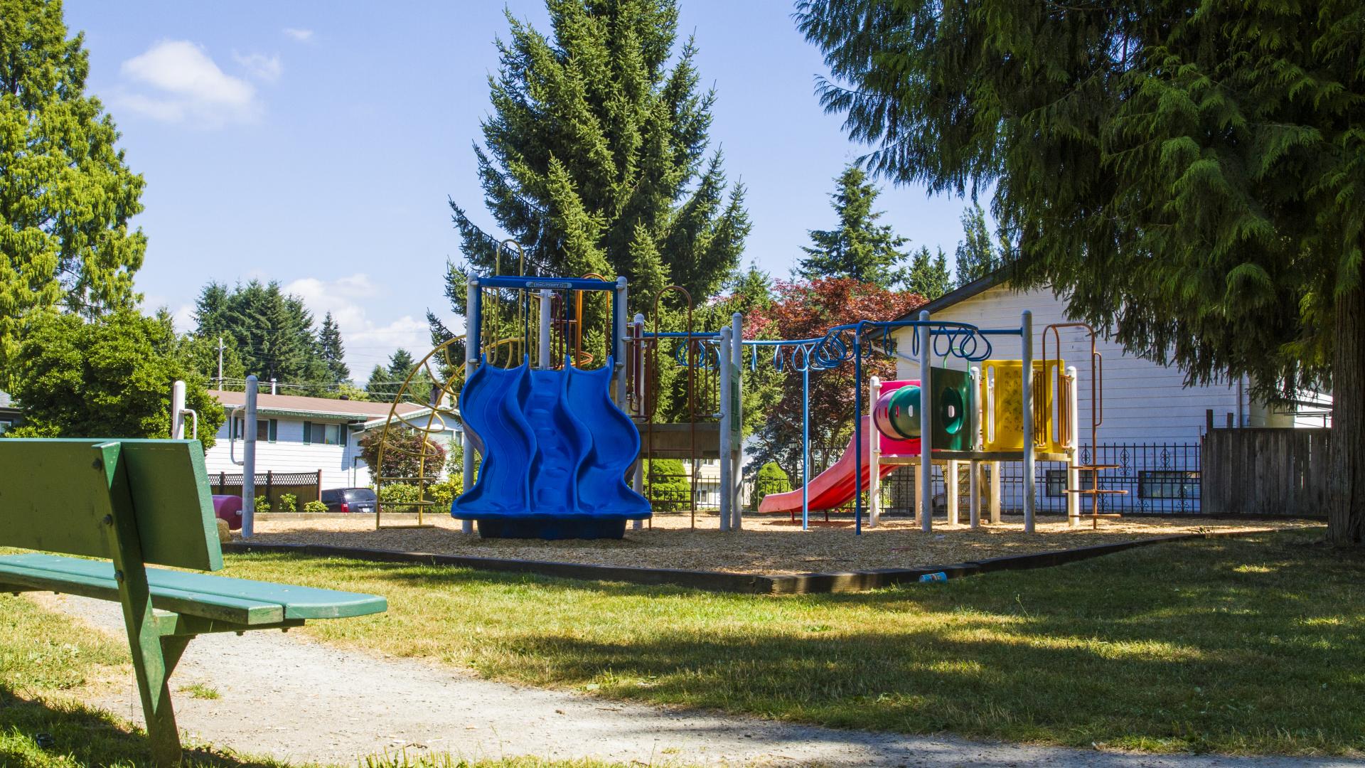 A small bench looks toward the playground, facing the blue slide directly.