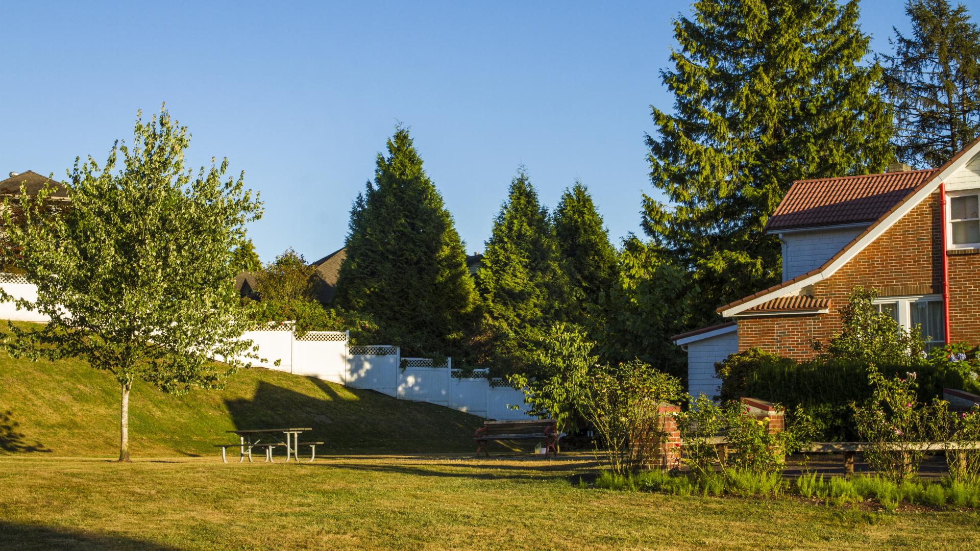 A grassy field with a picnic table in the back yard of a house. 