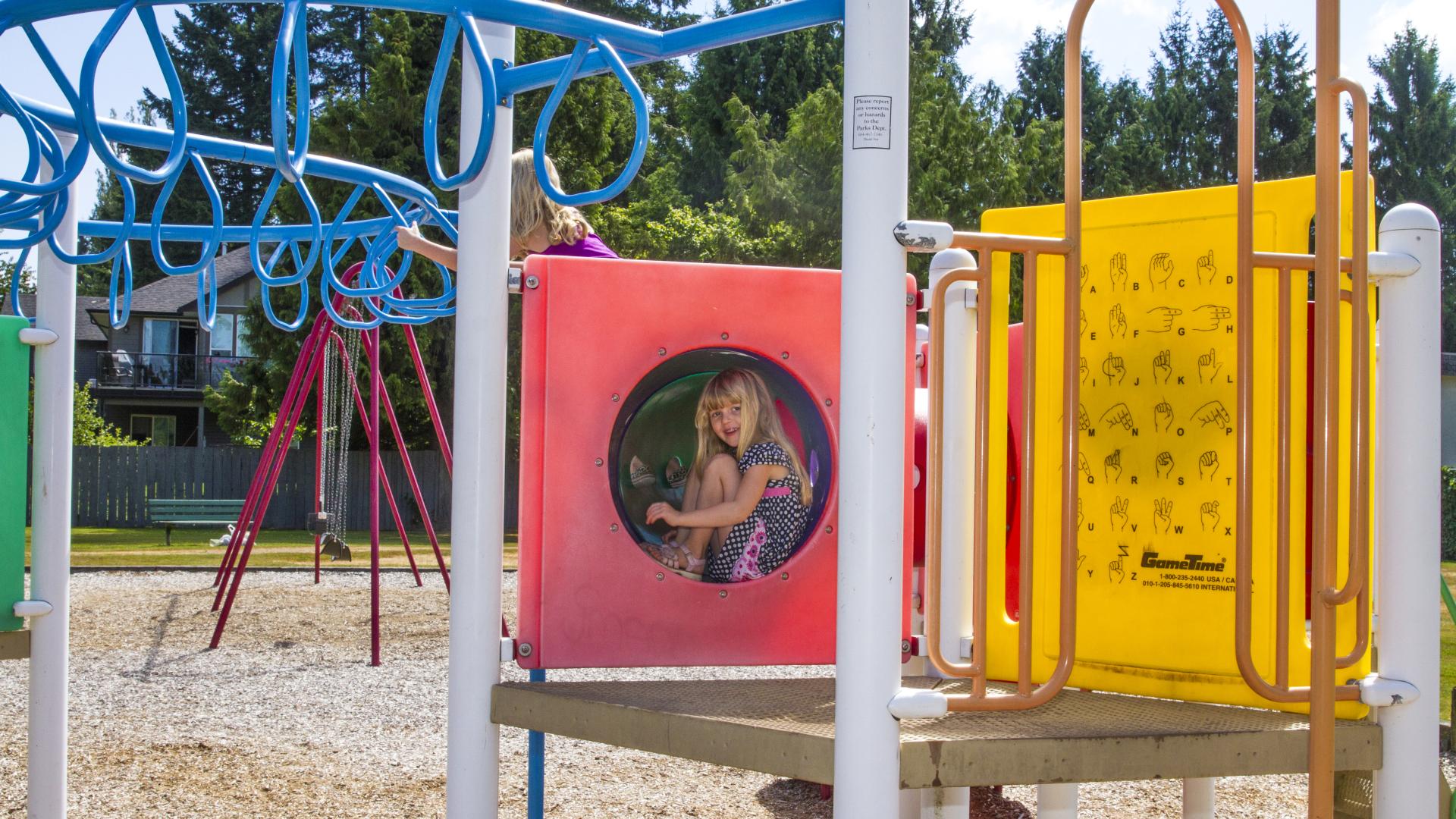 A young girls sits in the outcrop next to the monkey bars on a playground.