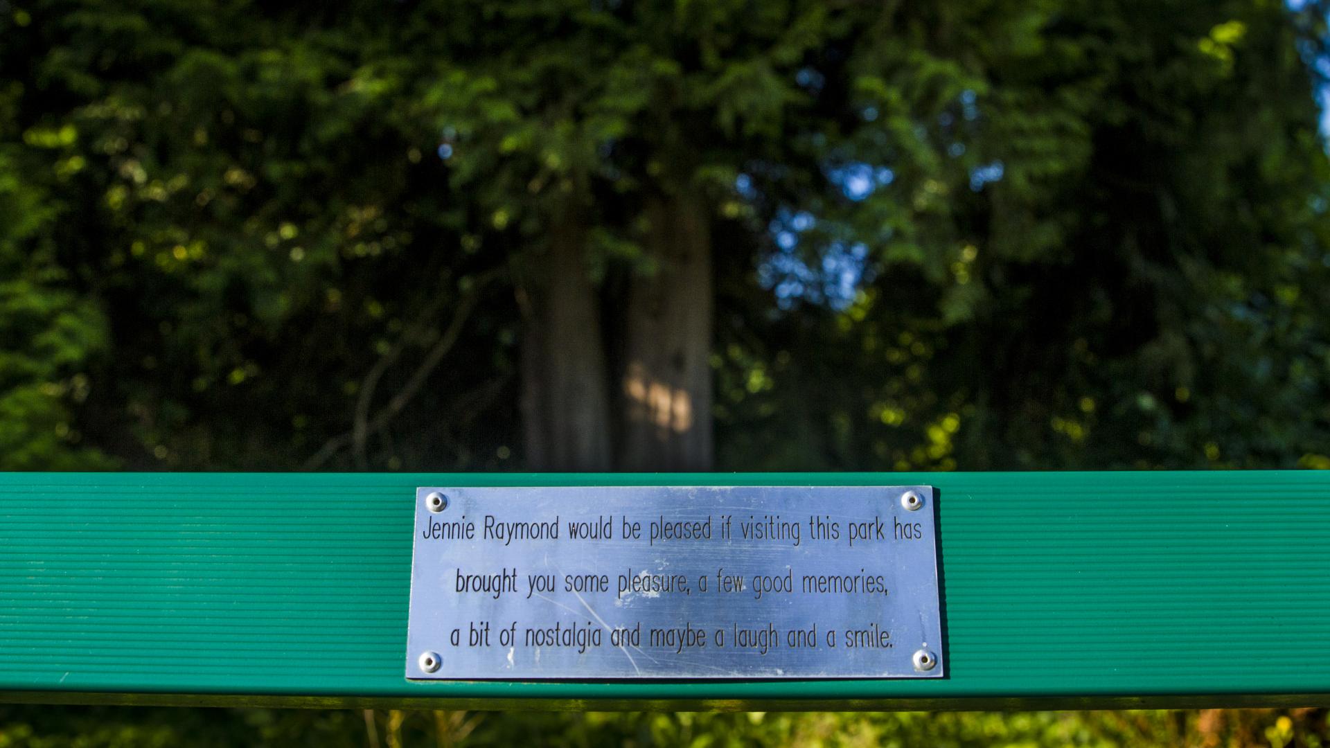 A dedication plaque on a bench that reads: "Jennie Raymond would be pleased if visiting this park has brought you some pleasure, good memories, a bit of nostalgia and maybe a laugh and a smile." 