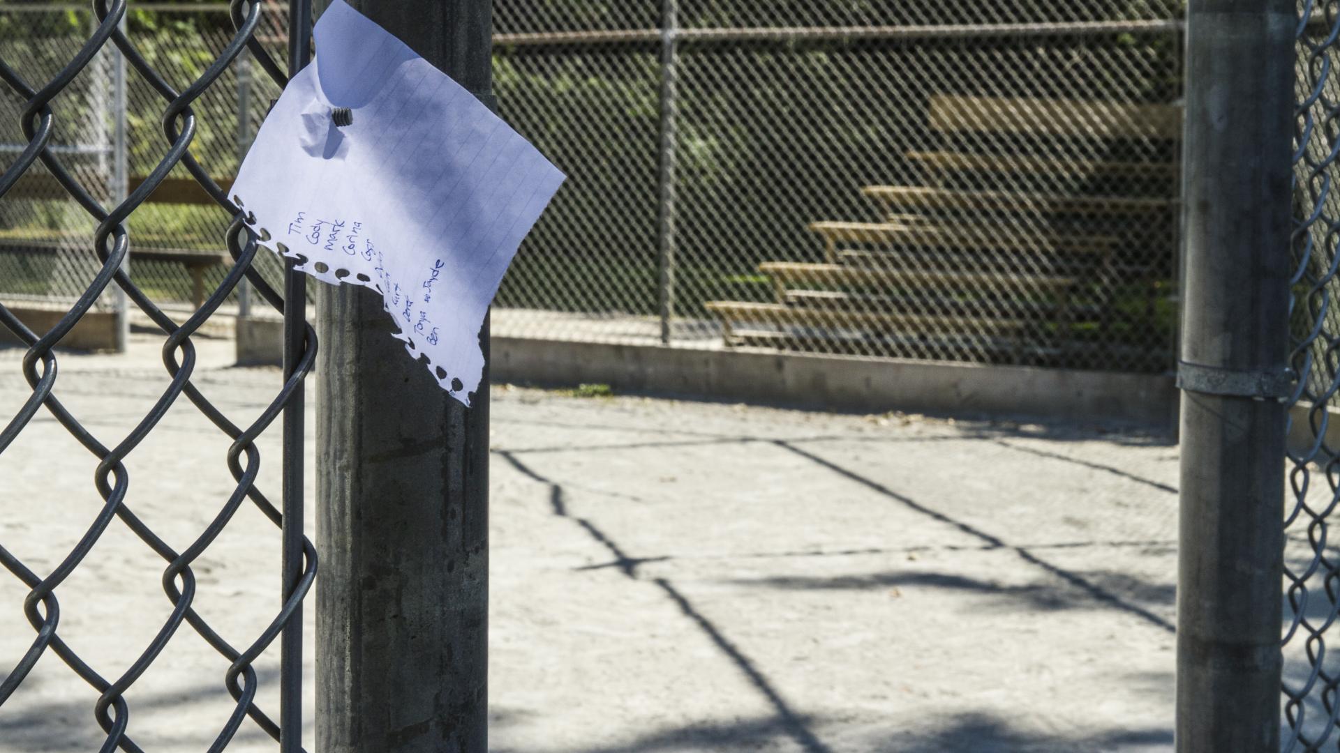 A paper note tacked to the entrance of a baseball diamond.
