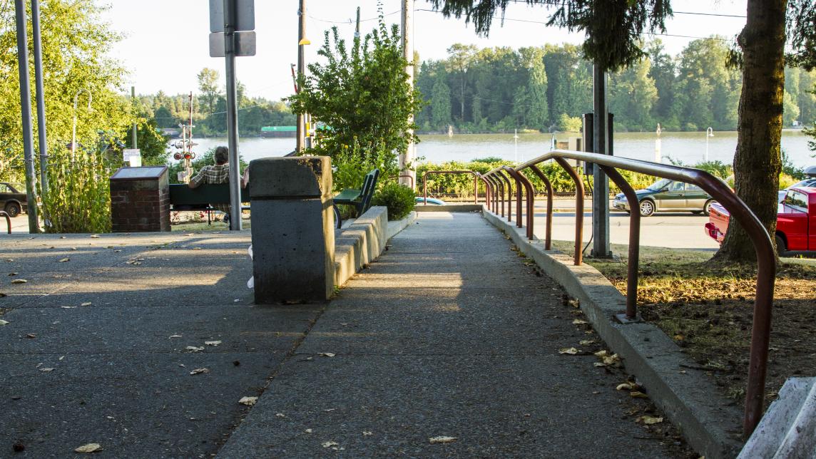 A sidewalk with a railing on one side leading toward the water.