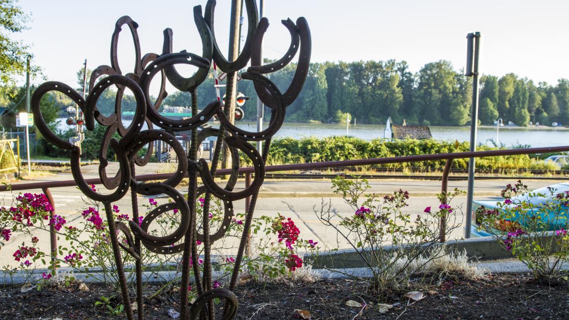 A branch mental sculpture near a road. Beyond that, there is a body of water.