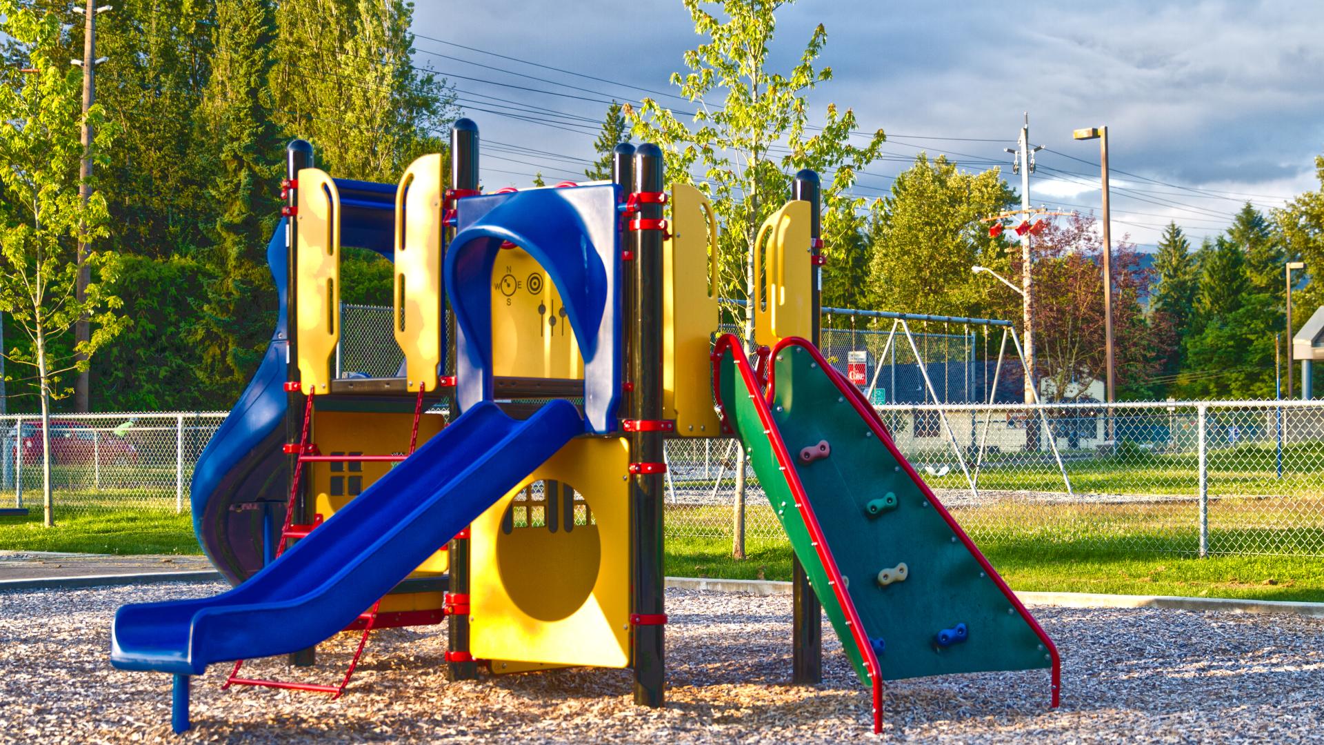 A playground with a few slides and a rock climb wall. Behind it, there appears to be a fenced in field.