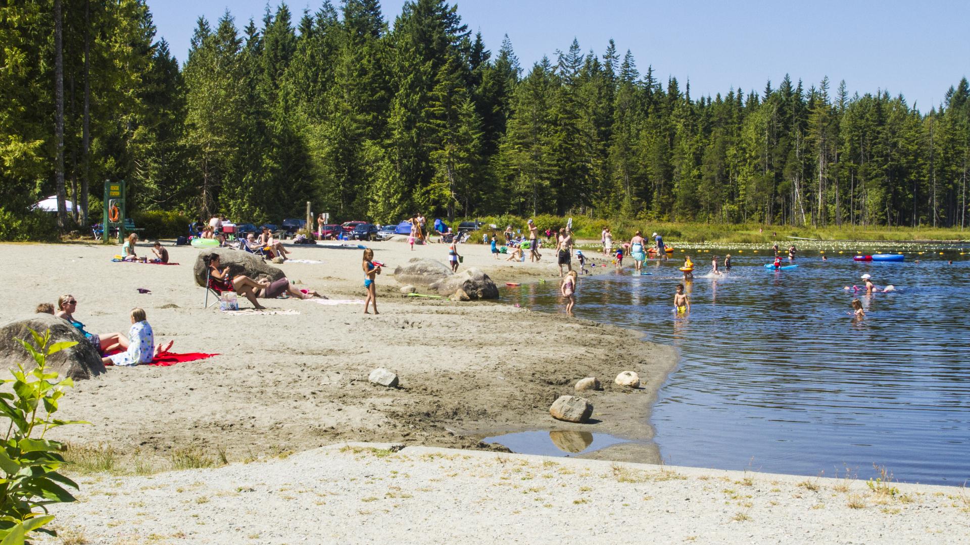 A busy beach with many people swimming in a lake.