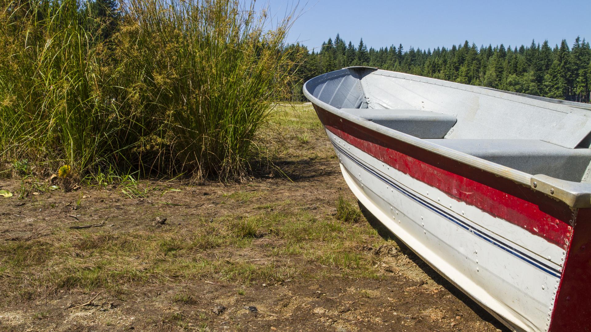 A red and white row boat sits on a muddy grassy patch.