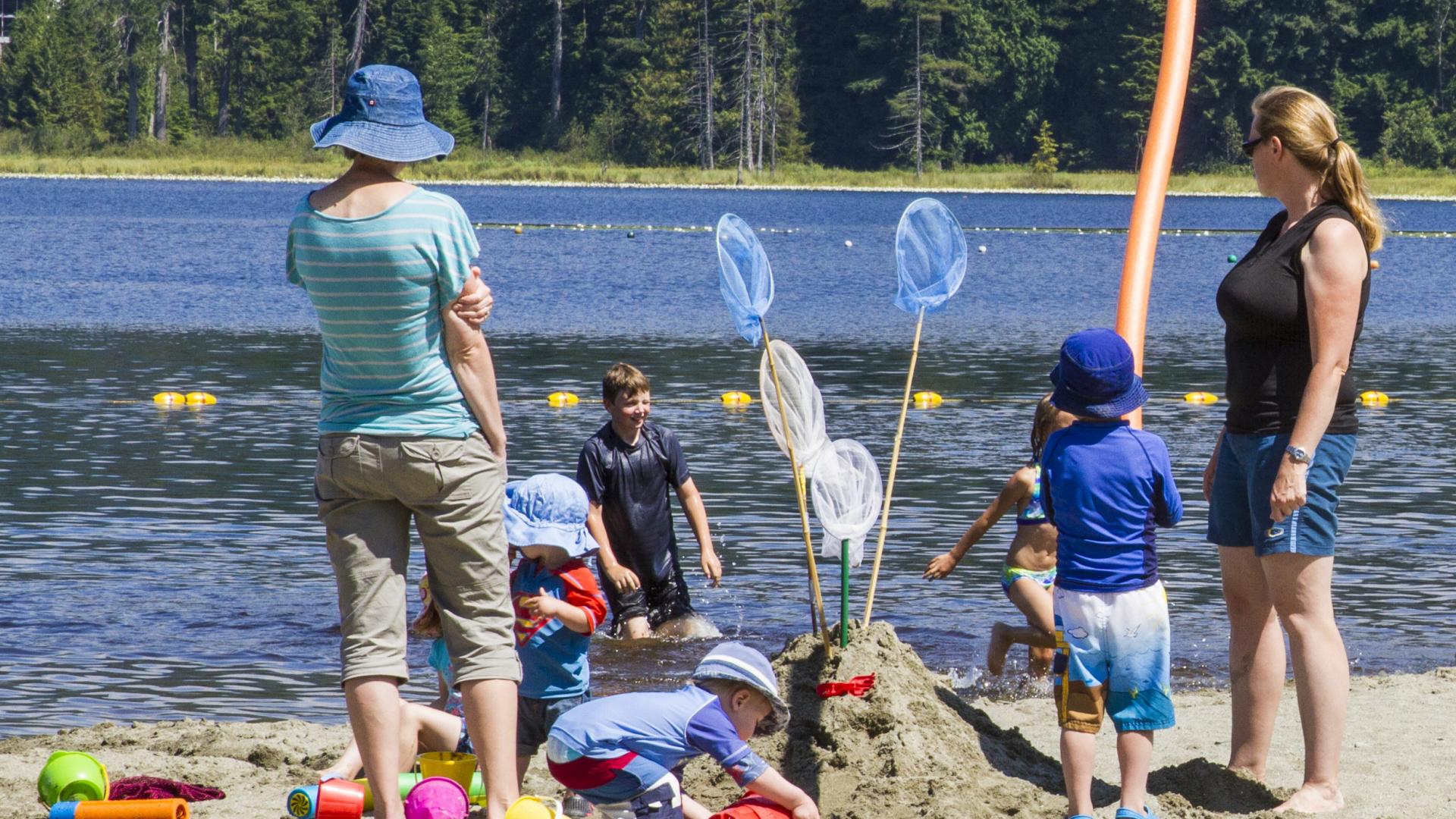 A family stand on the beach. Some kids are building a sand castle, decorated with bug nets.
