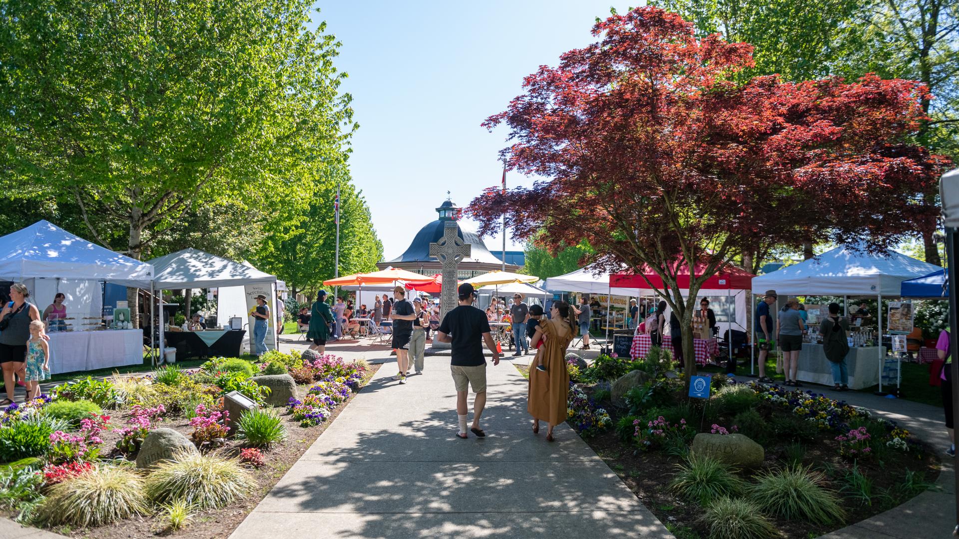 Couple walking down the path of Memorial Peace Park passing by booths at Haney Farmers Market
