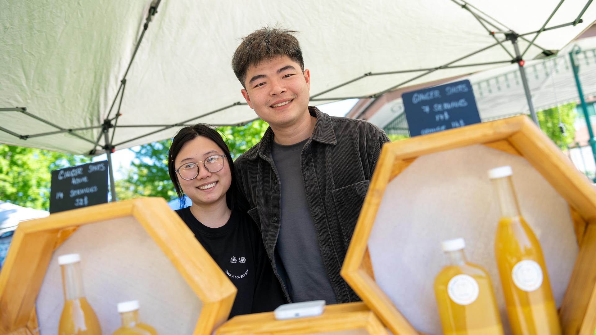 Woman and man standing behind a tower of juice product eager to sell to interested customers