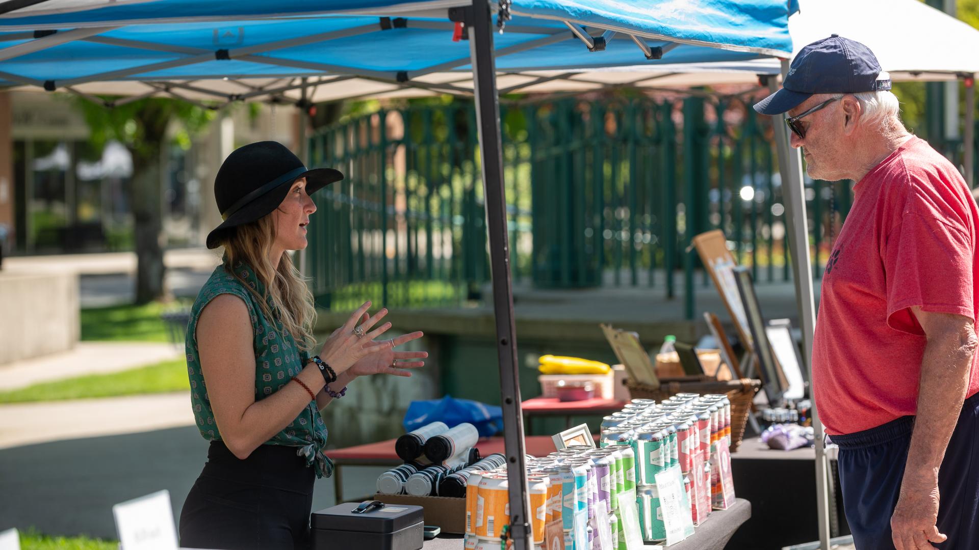 Women standing behind a booth at the Haney Farmers Markets selling juice to an interested consumer