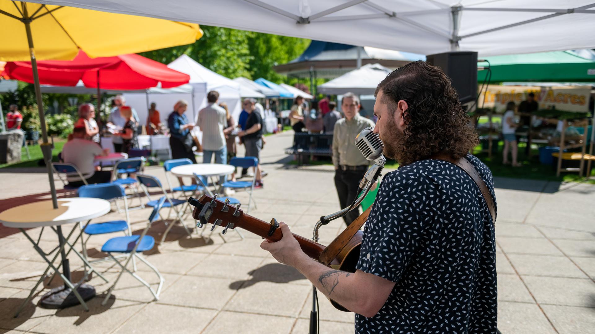 Man playing guitar and singing to a moderate crowd who are shopping at the Haney Farmers Market