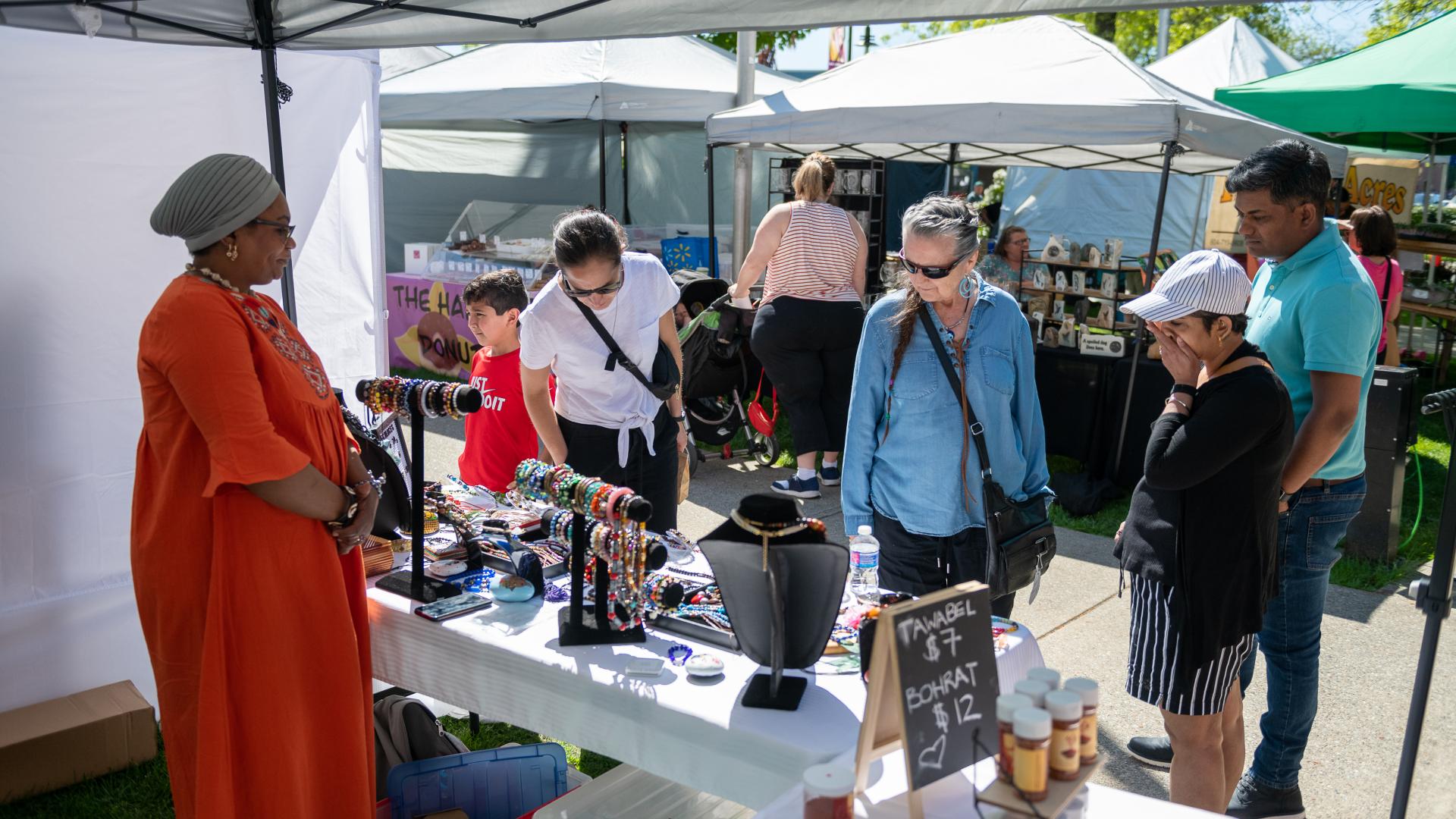 Women standing behind booth selling beautiful pieces of jewelry to interested customers at the Haney Farmers Market