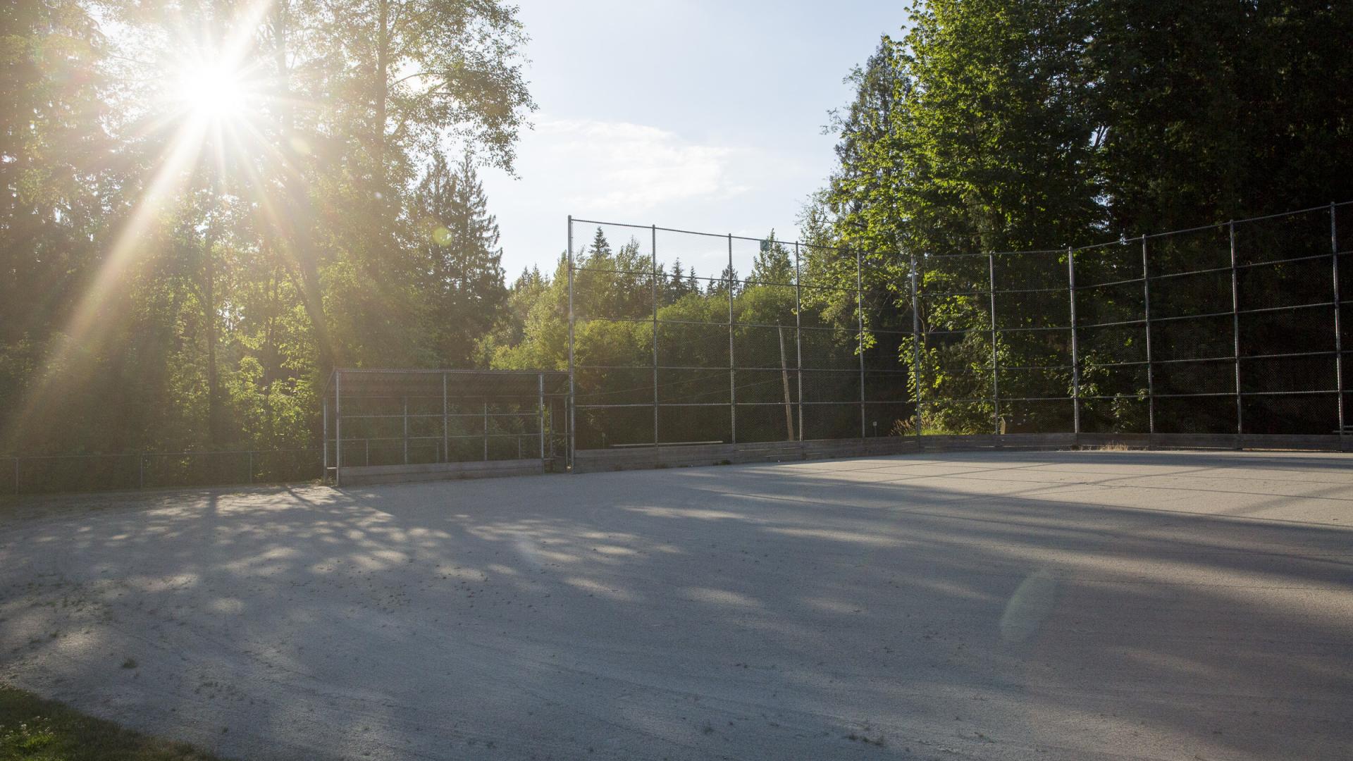 The sun peaks through the trees overshadowing a baseball diamond.