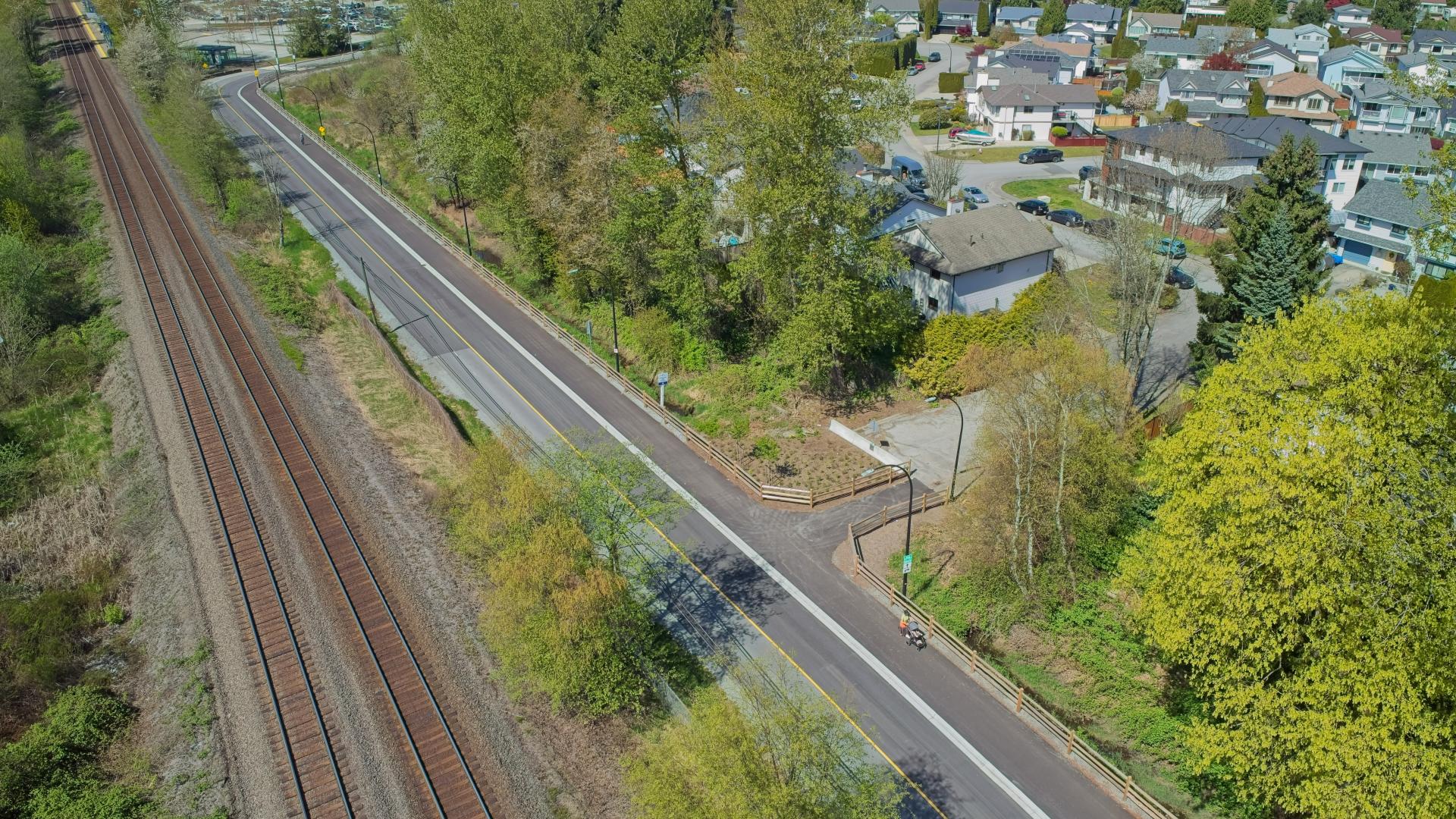The Hammond Multi-Use Path runs parrallel to a set of train tracks through a greenspace. There are houses in the distance.