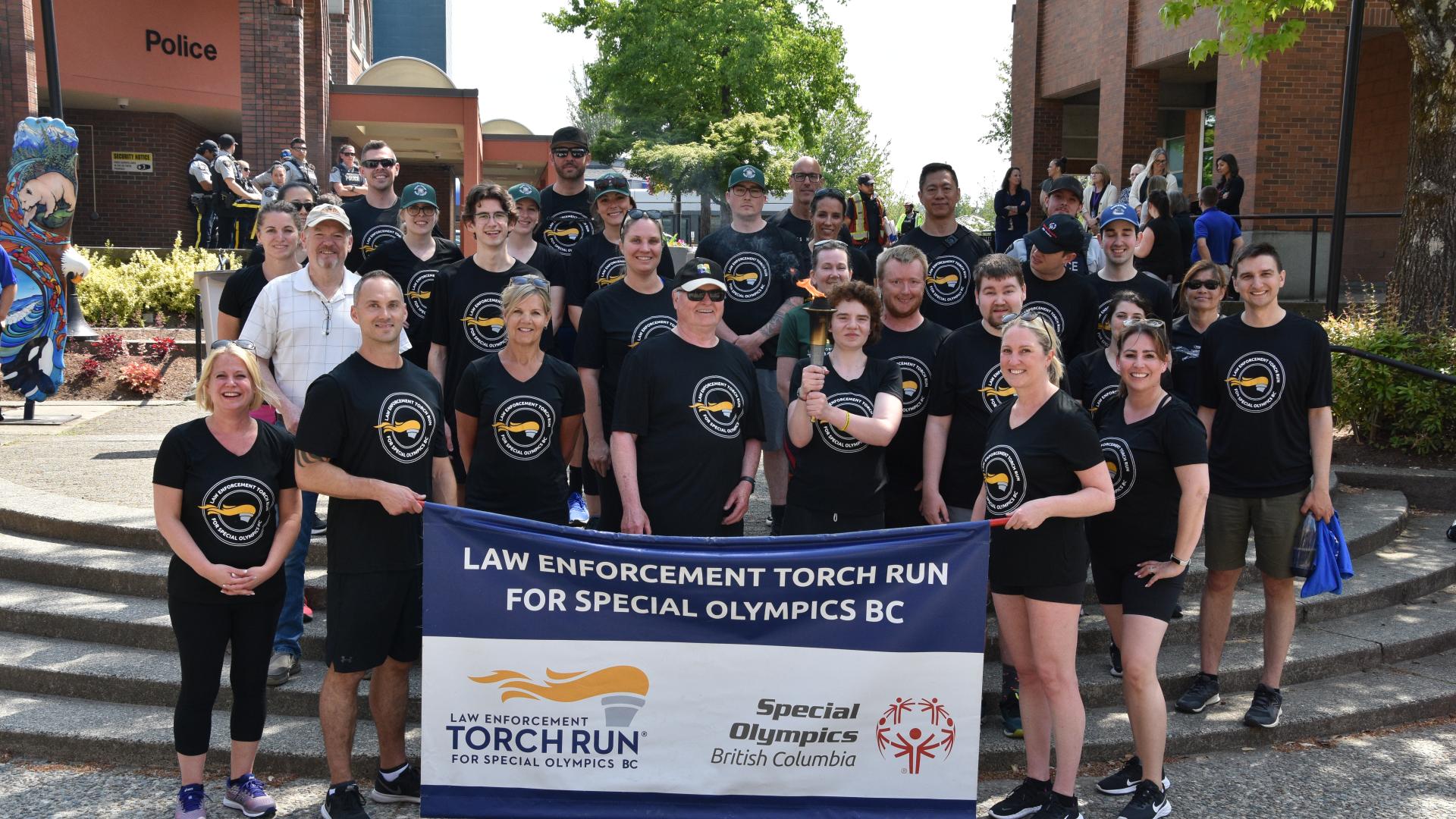 Crowd of people standing spread out on stairs posing, holding a Law Enforcement Torch Run banner after completing the Law Enforcement Torch Run