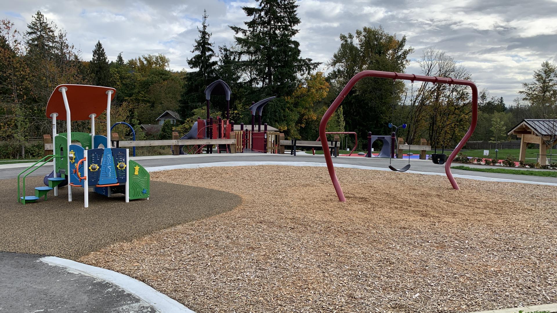 A red single-barred swing-set with one toddler seat and one flat seat sits next to a small toddler playground in vibrant blues, greens and yellows.