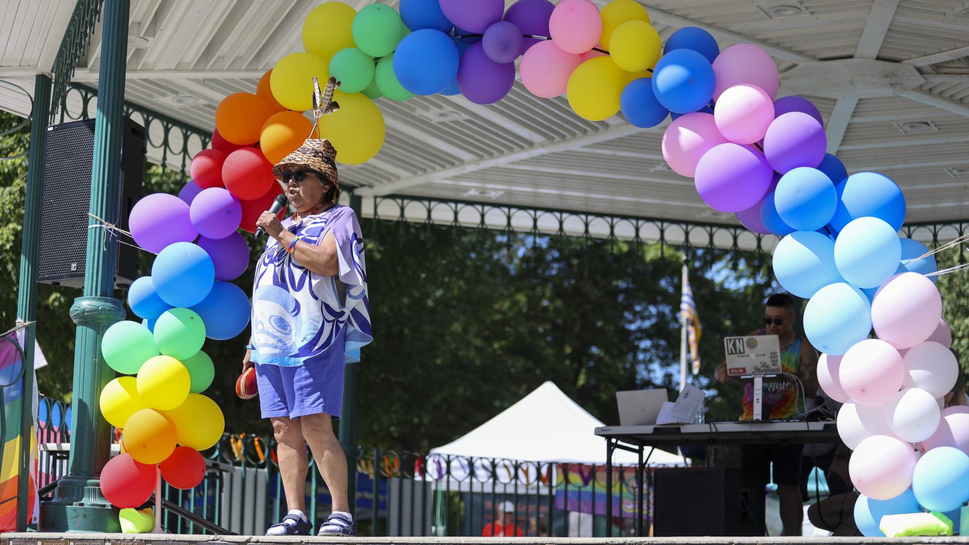 Woman giving a speech to a crowd with a rainbow balloon arch above her head