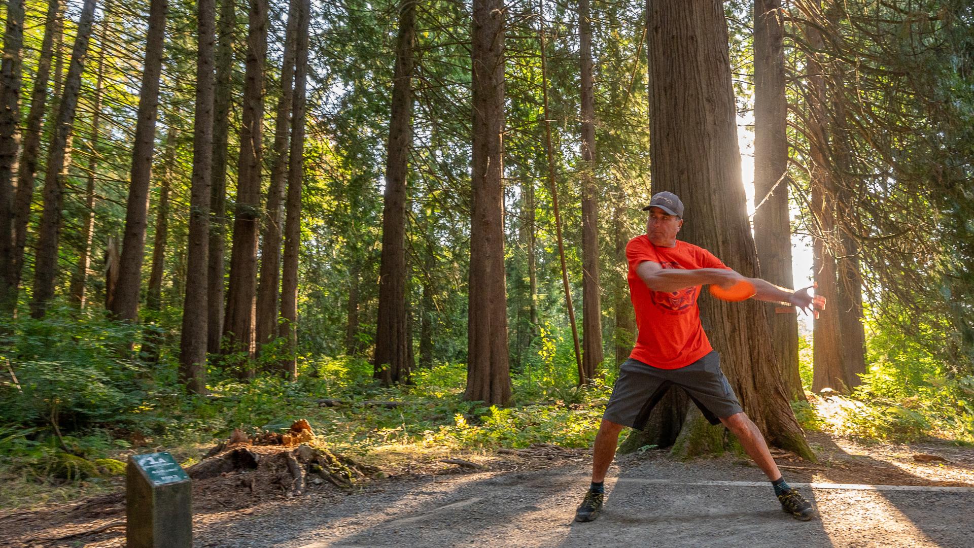 A man winds up to throw a frisbee for a game of disc golf surrounded by trees.