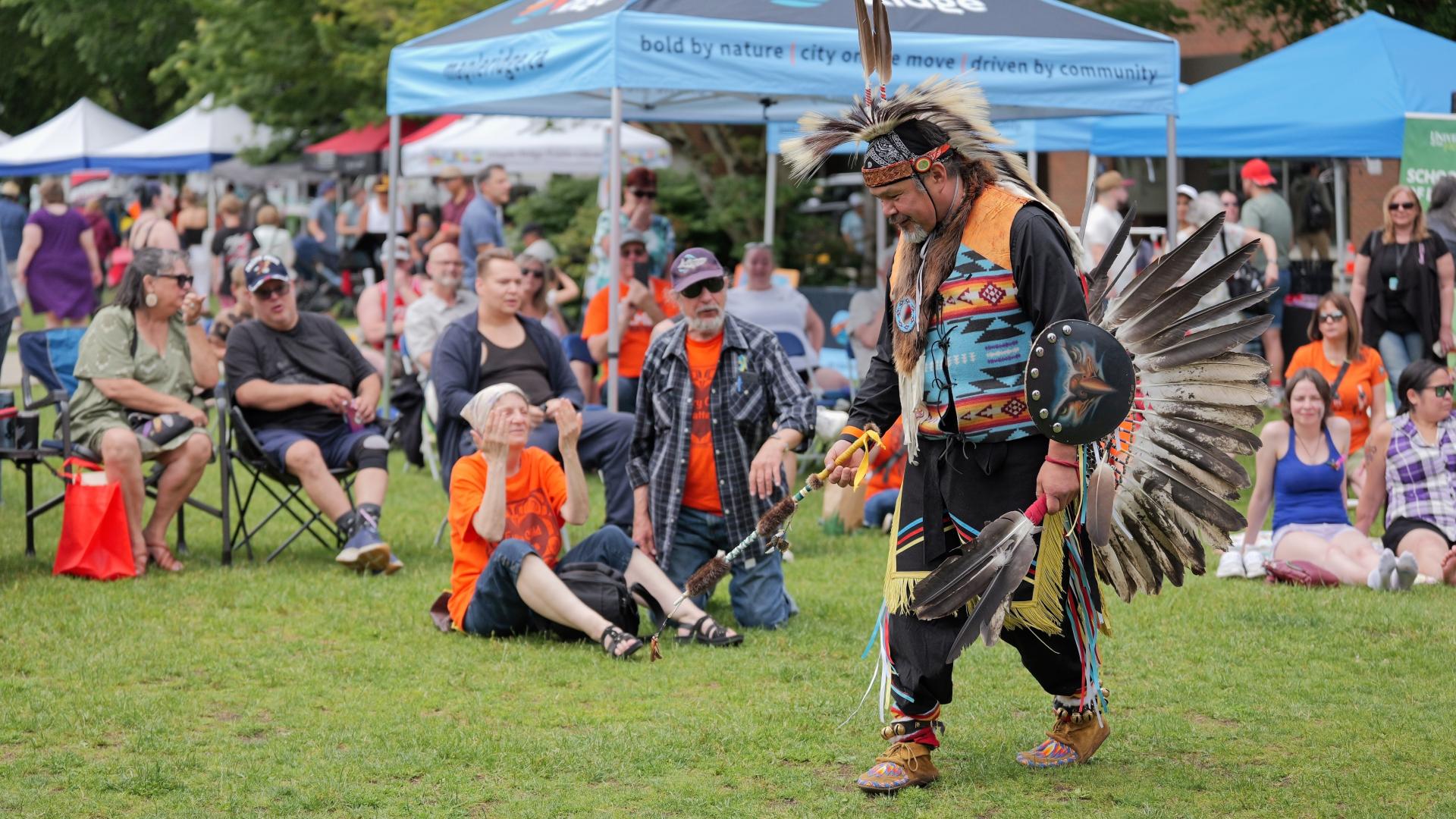 A First Nations man in ceremonial dress gives a presentation at National Indigenous Peoples' Day festivities in Memorial Peace Park