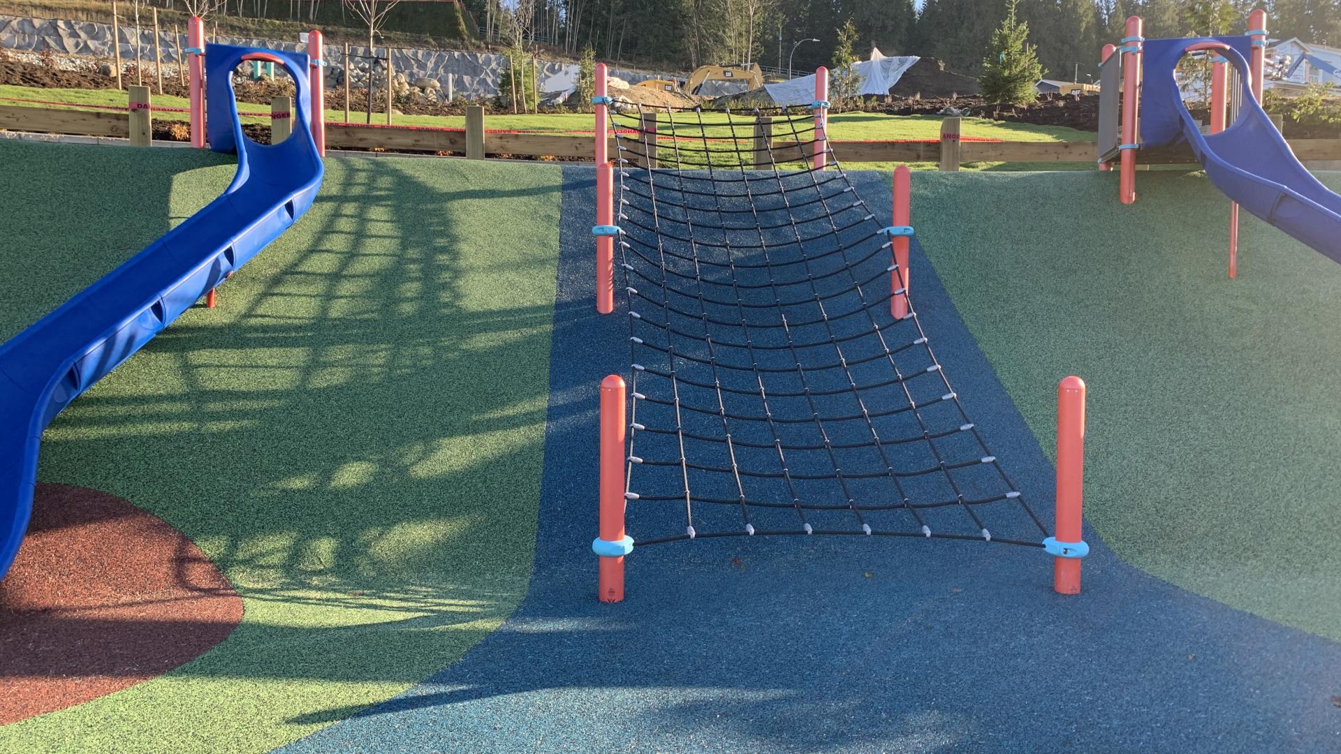 Net climber up rubber surfaced hill with slides beside
