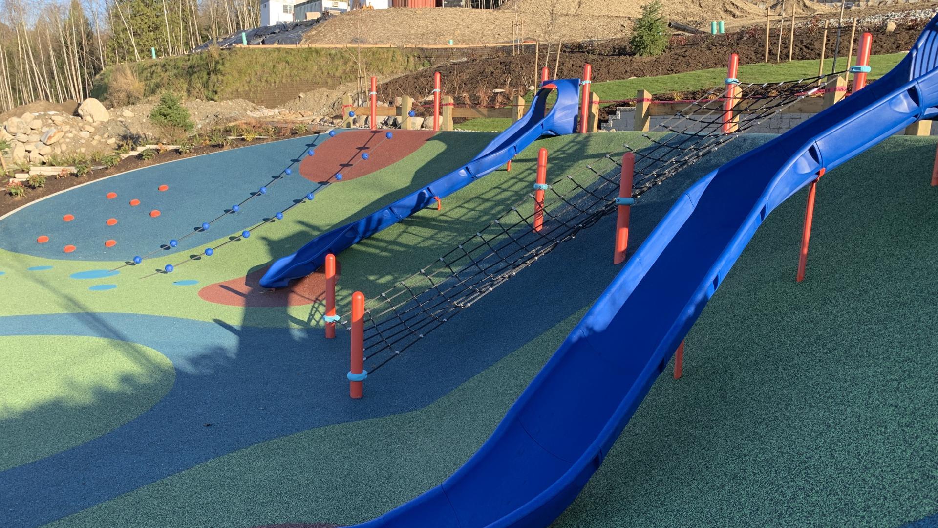 Blue plastic slides down rubber surfaced playground hill with net climber up hill