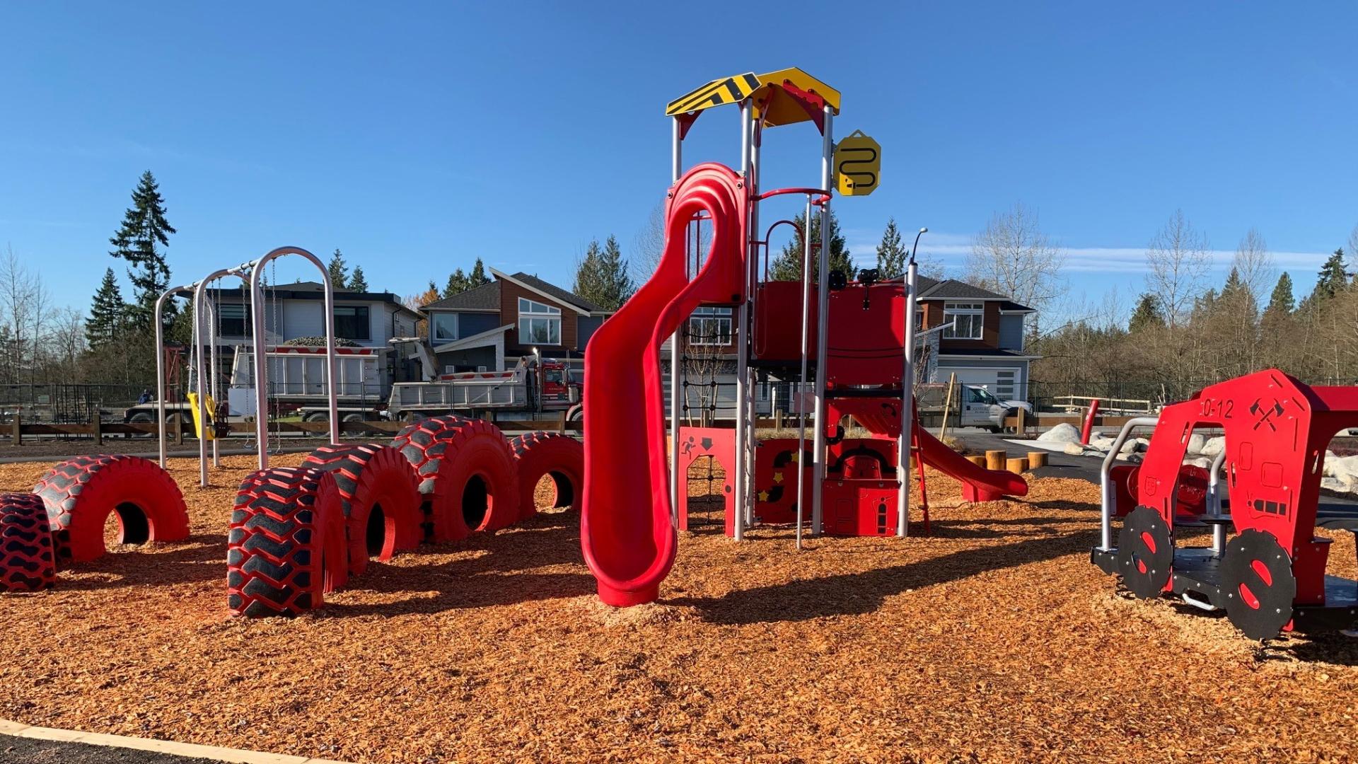 Red playground with slide, tires and play house on woodchip surfacing