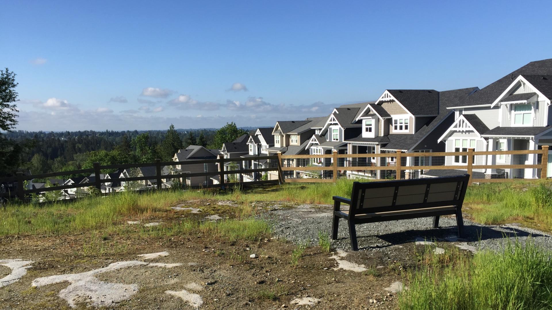 Bench on hill overlooking view with houses to the right