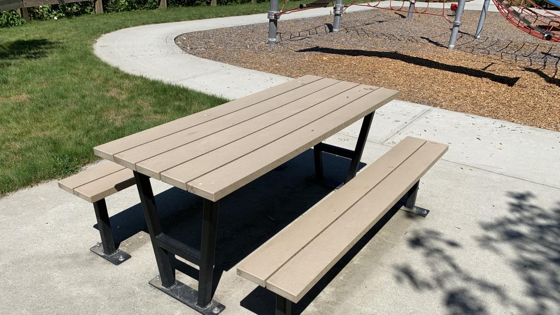 Picnic table on concrete pad with sidewalk and playground behind