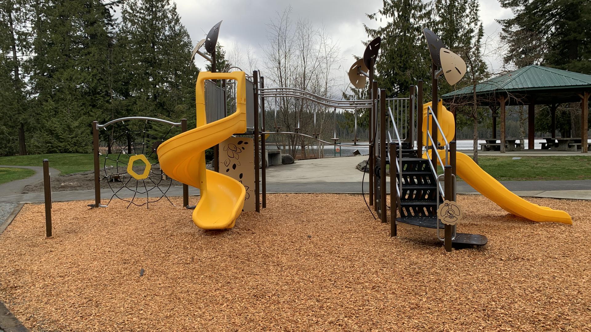 new playground structure with two yellow slides and a large sand area in the background